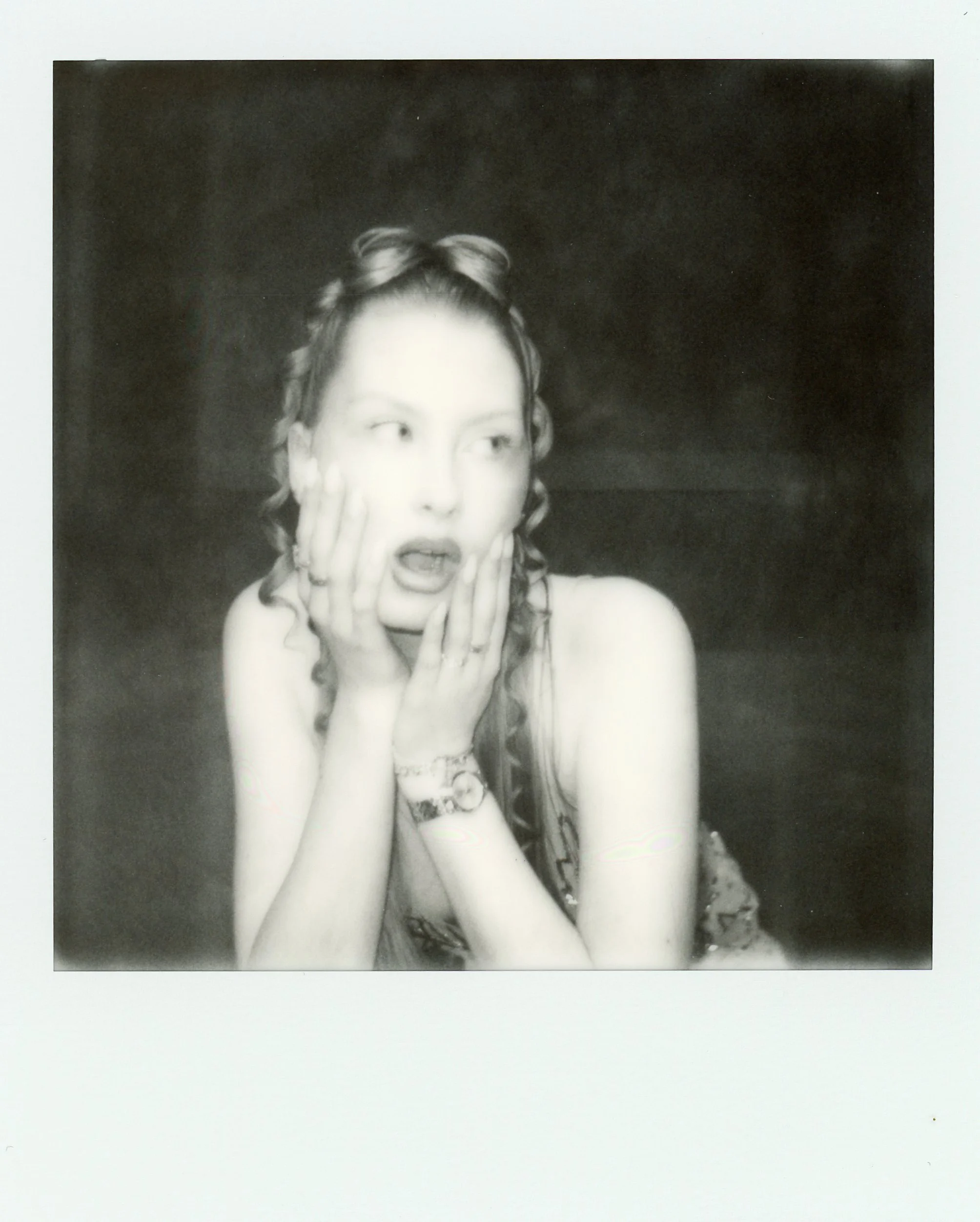 Une femme avec des cheveux bouclés et un bracelet, ayant une expression de surprise ou d'étonnement, avec les mains sur le visage.