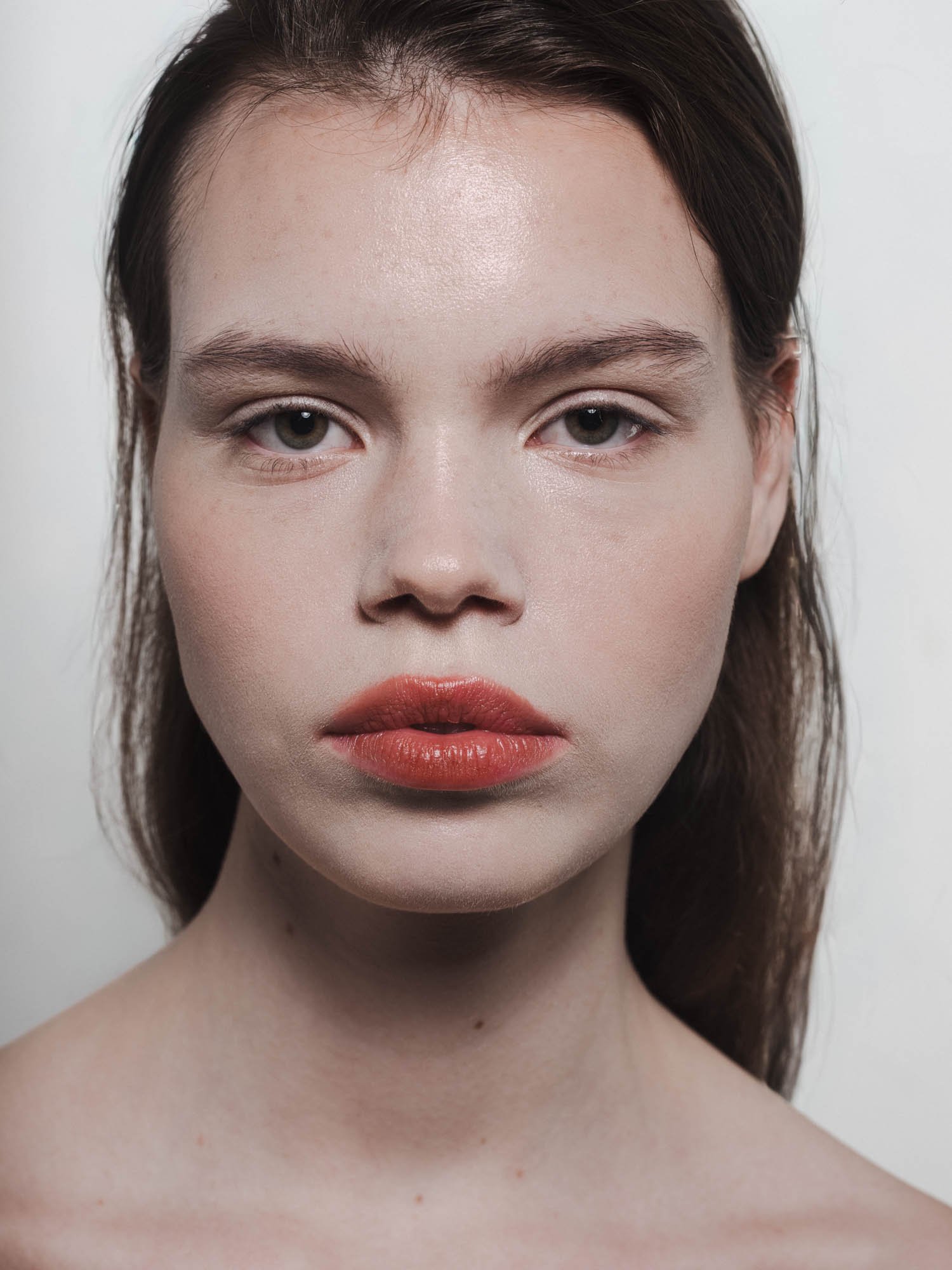 Portrait d'une jeune femme avec une peau claire, des lèvres rouges et des yeux gris, regardant directement l'objectif.