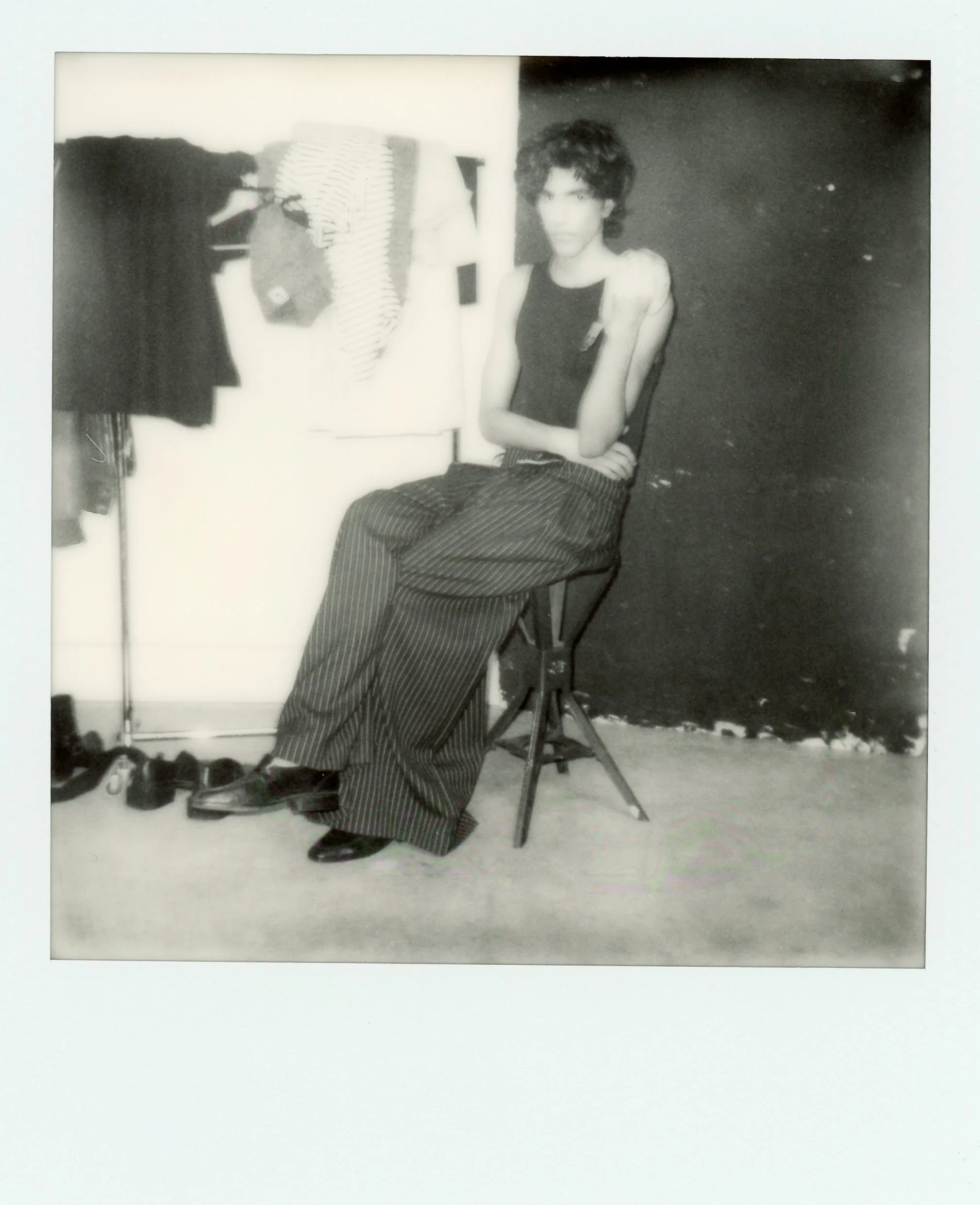 Une jeune femme assise sur une chaise en studio, portant un haut noir et un pantalon à rayures, dans une ambiance rétro en noir et blanc.