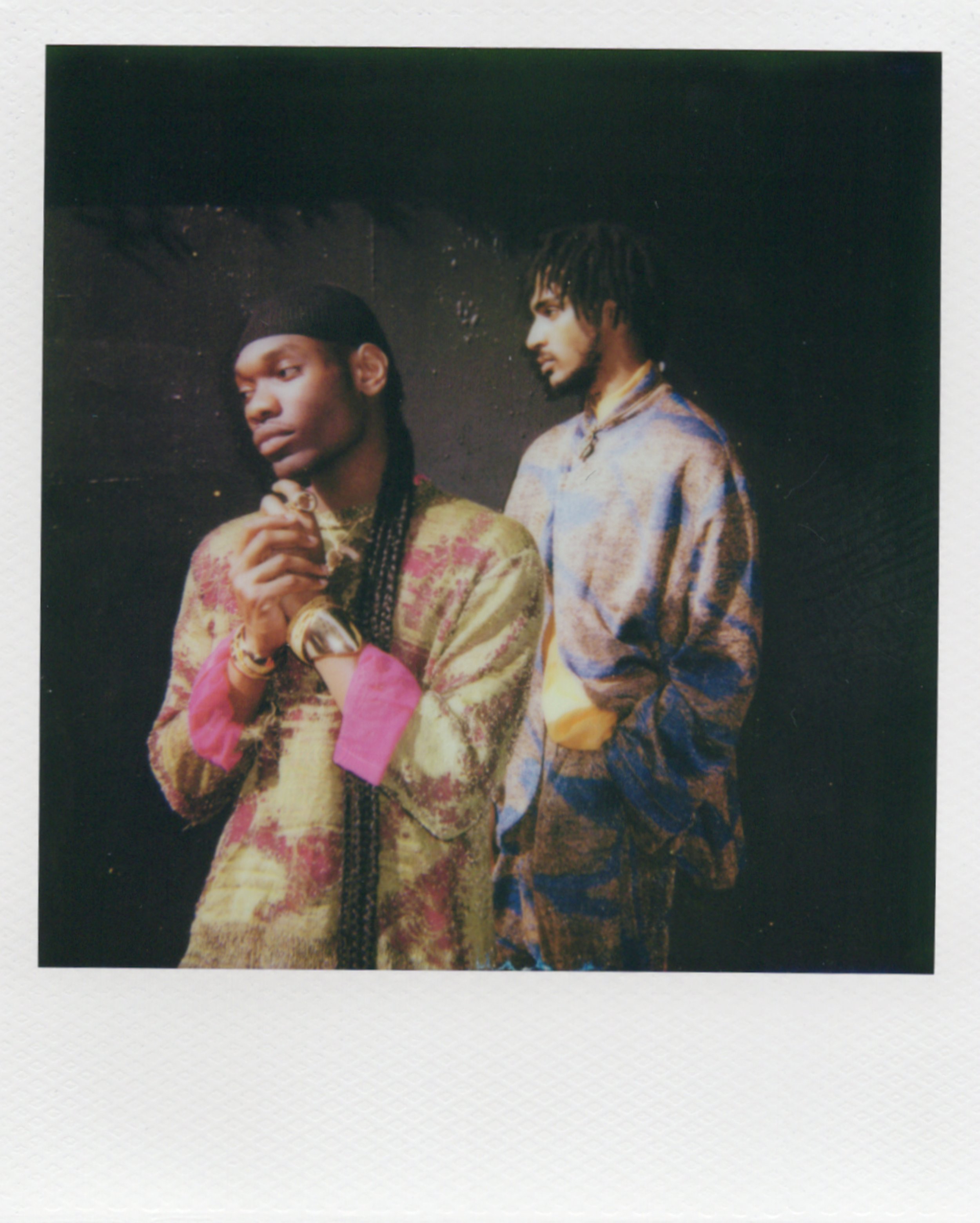Deux jeunes hommes portant des vêtements colorés et à motifs, posant sur un fond sombre.