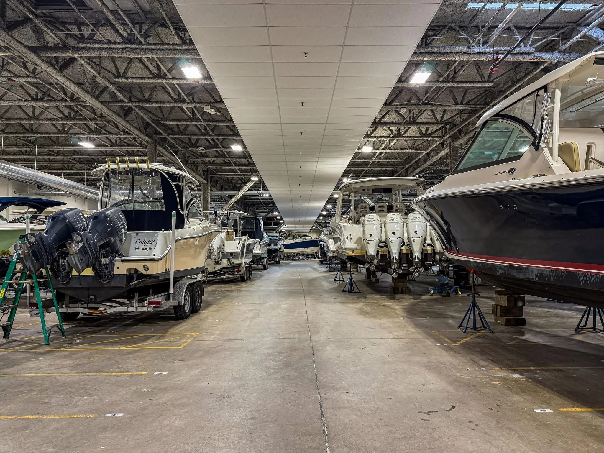 Indoor boat showroom with multiple boats on trailers, including a black and red boat on the right and several white boats with engines in the center and left.