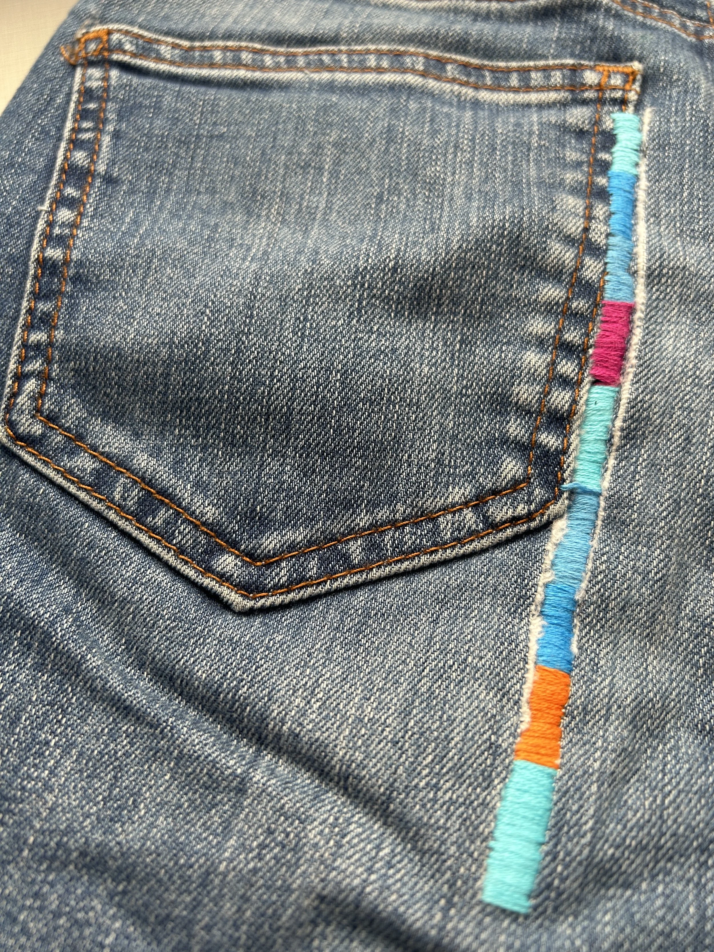 visible mending on denim jeans with bright coloured embroidery thread