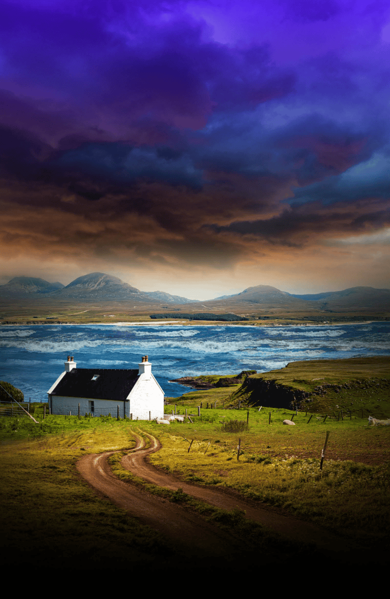 A rural house with a black roof and white walls surrounded by green fields, dirt driveway, fences, and a view of the ocean with waves, distant mountains under a dramatic sky with dark purple and orange clouds.