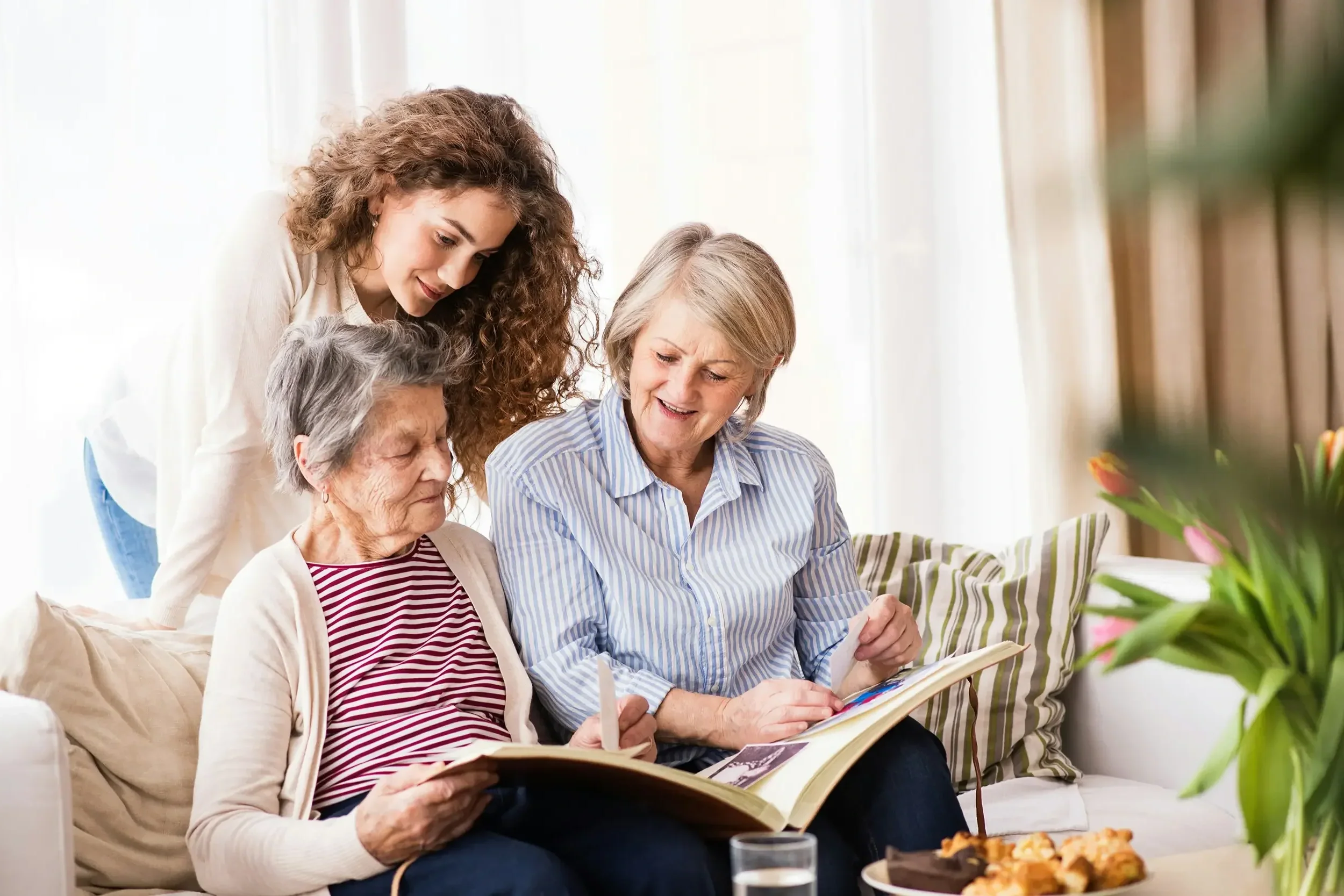 Three women sitting on a couch looking at an album after ancestral lineage healing.