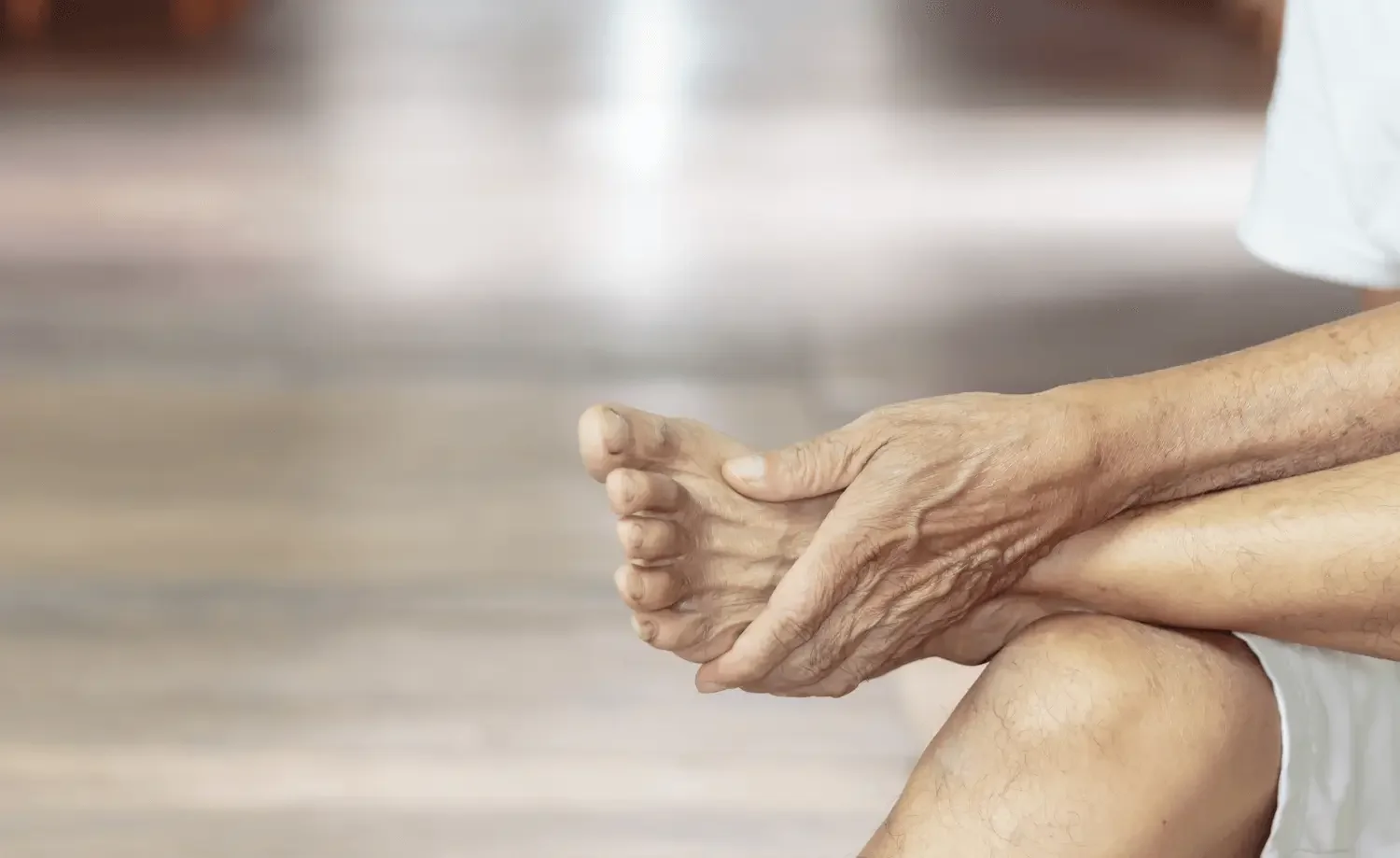 Close-up of elderly person's hand holding their foot because of tingling due to peripheral neuropathy.
