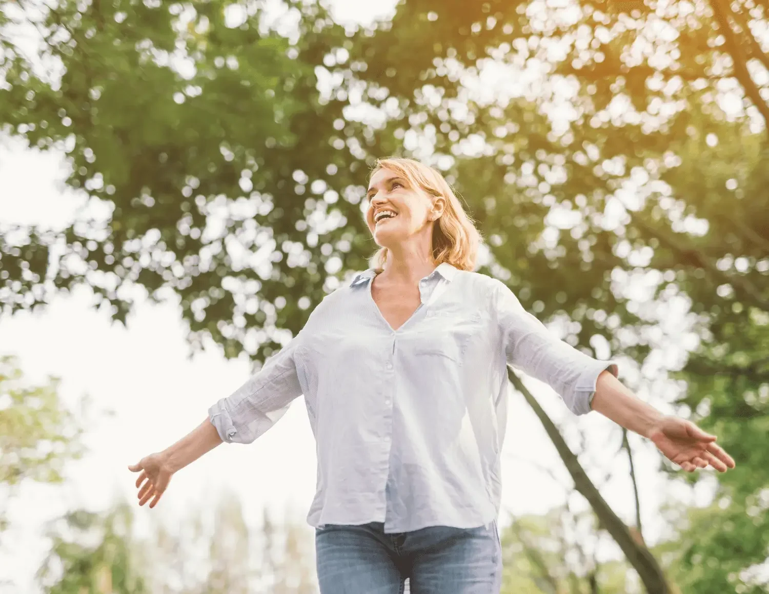A woman with blonde hair smiling and enjoying outdoors with arms outstretched in a park in Aspen, CO.