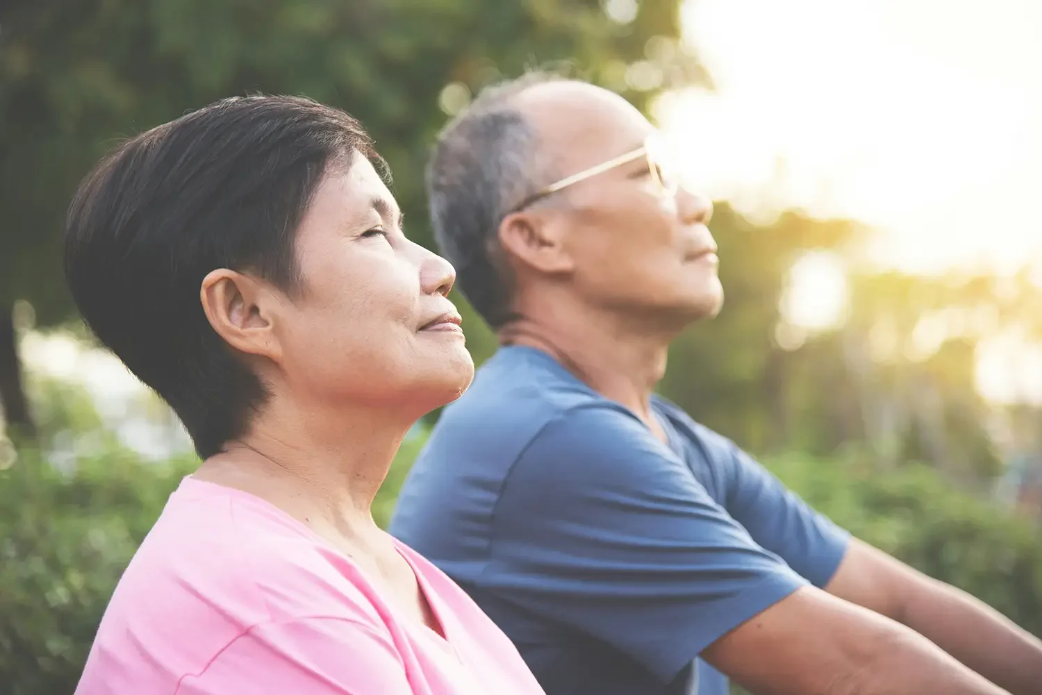 An older woman and man sitting outdoors with eyes closed, enjoying sunlight and nature after cancer support with Zelena Medicine.
