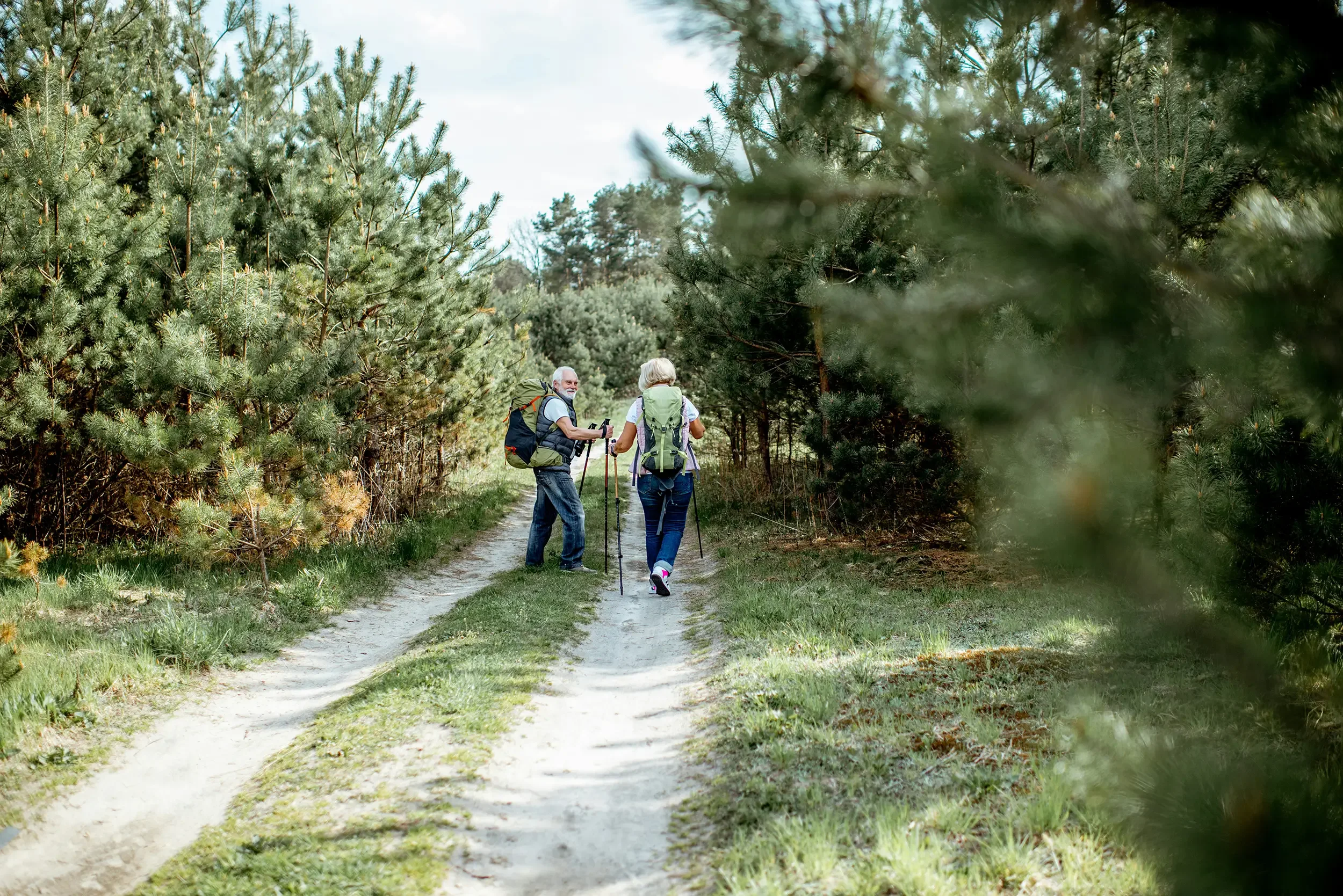 Two seniors with backpacks and hiking poles walking on a forest trail in Aspen, Colorado.