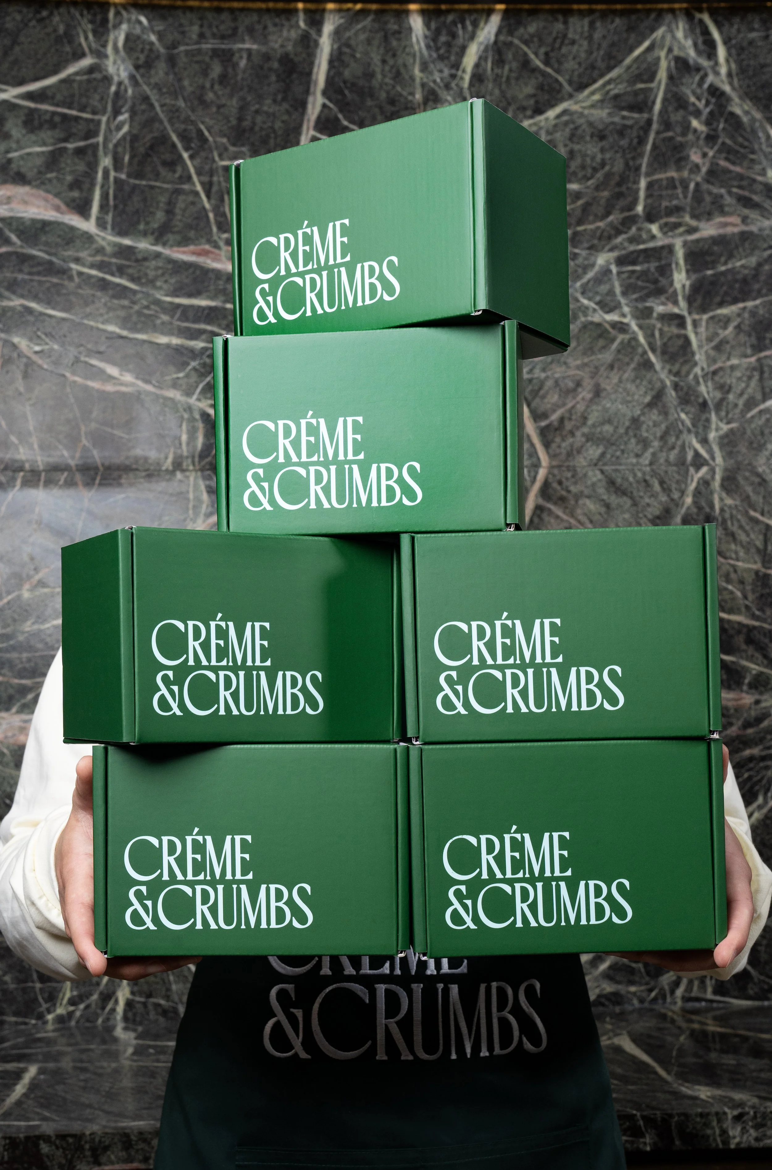 Photo of a pile of 6 green boxes with the light green "Créme & Crumbs" logo on it