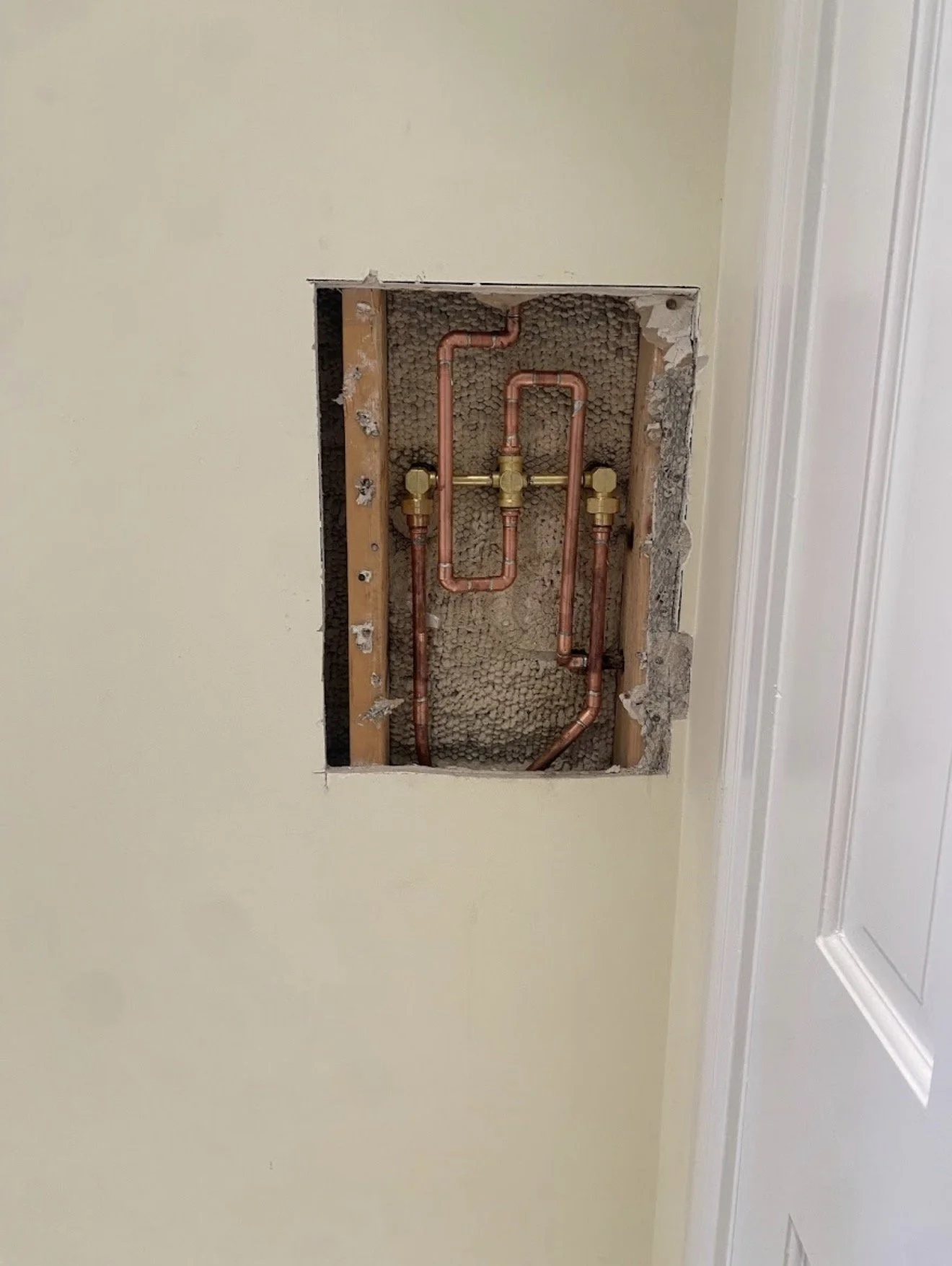 Open wall with copper plumbing pipes and fittings inside a wall cavity