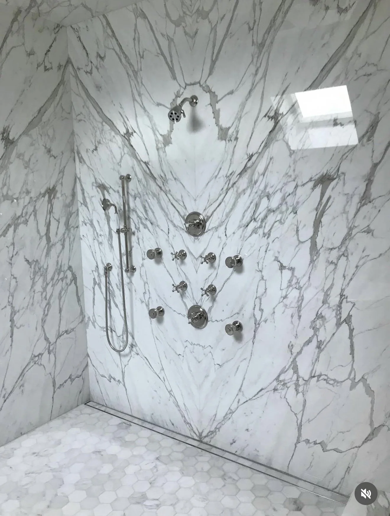 Marble shower with multiple chrome shower heads and controls on marble wall.