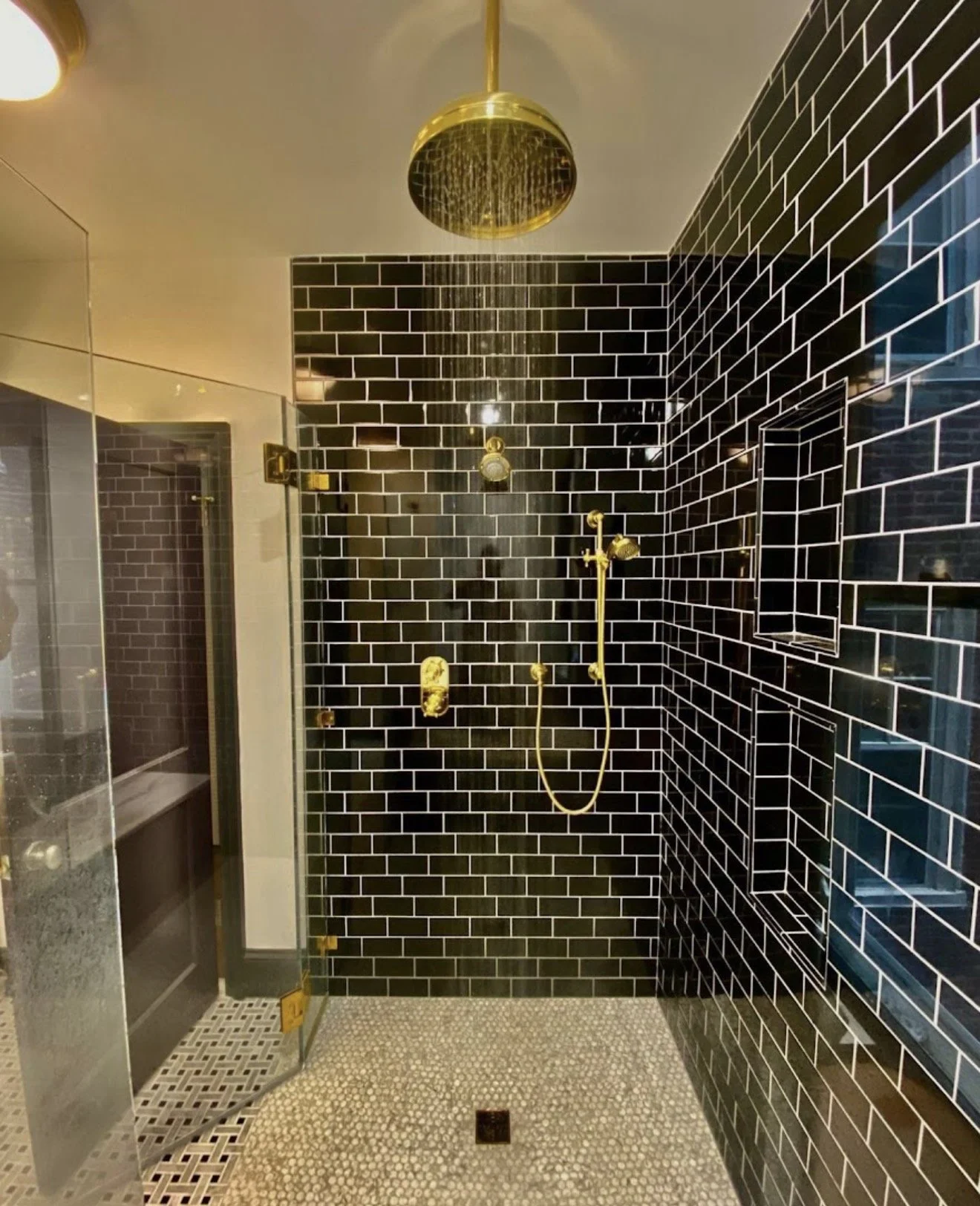Modern shower with black subway tiles, gold fixtures, and pebble stone floor.