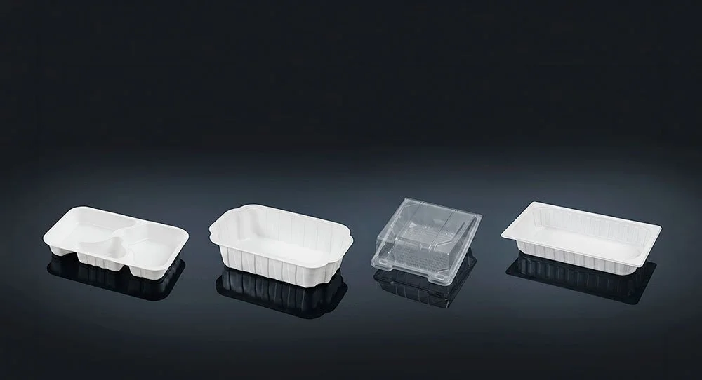 Fyra olika plastmatbehållare på en svart yta, inklusive en med två sektioner, en stor, en mindre transparent, och en rektangulär.