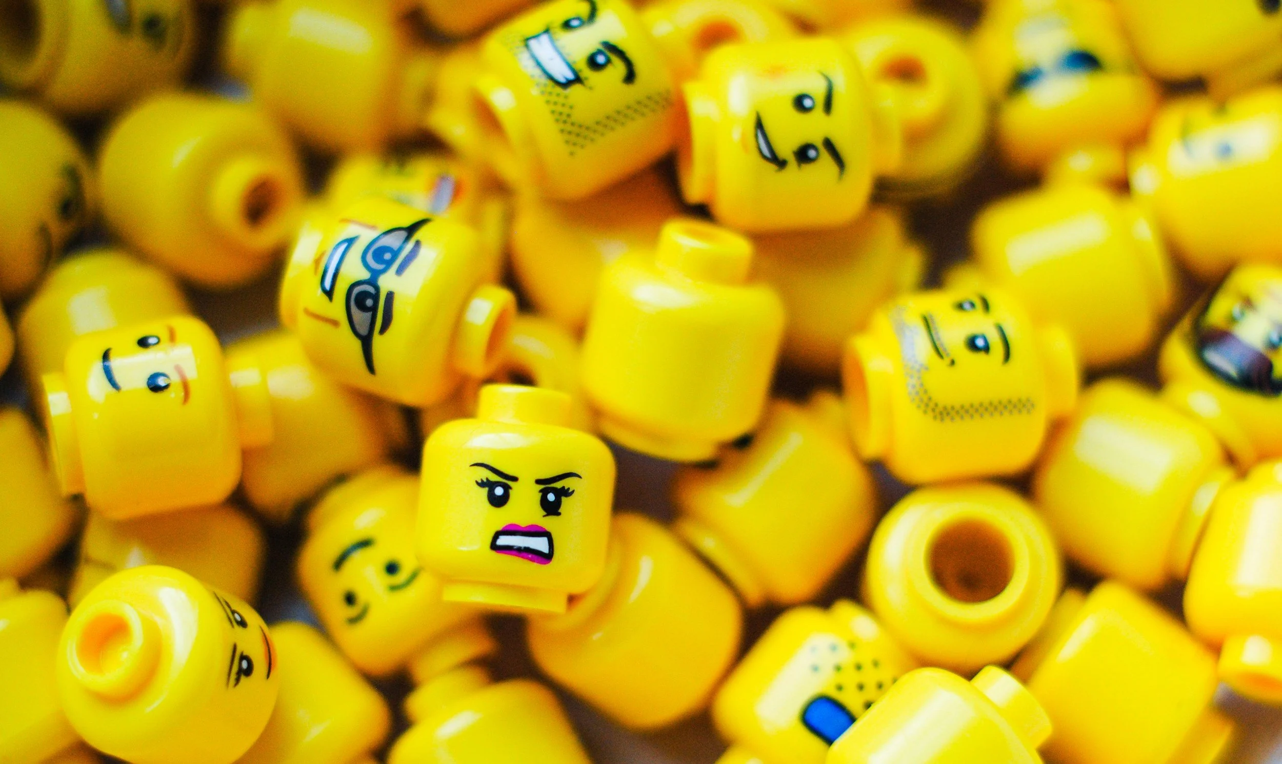 A pile of small yellow LEGO minifigure heads with various facial expressions.