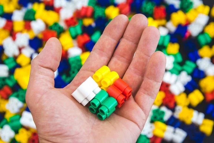 Close-up of a hand holding small colorful building blocks in front of a pile of similar blocks.