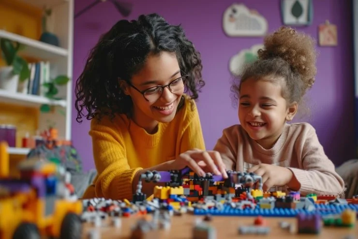A woman and a young girl playing with colorful building blocks at a table in a room with purple walls.