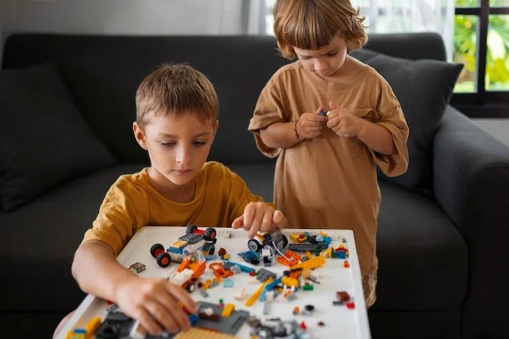 Two young boys playing with LEGO toys at a white table in a living room.