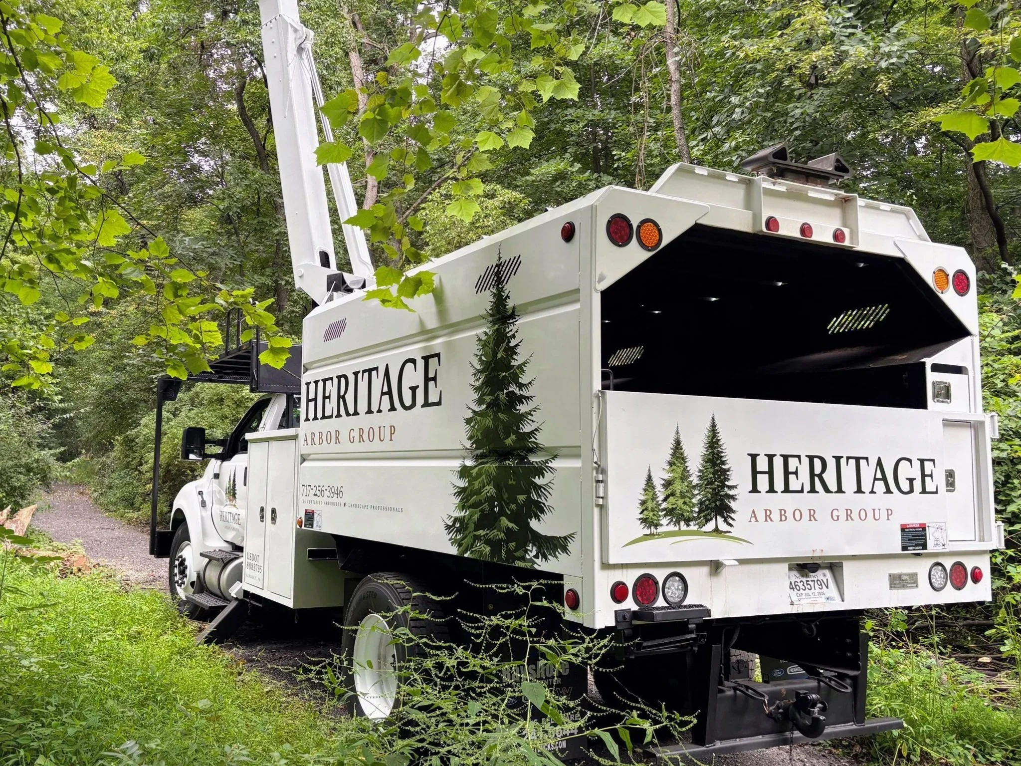 White Heritage Arbor Group service truck parked on a grassy and dirt path surrounded by green trees and foliage.