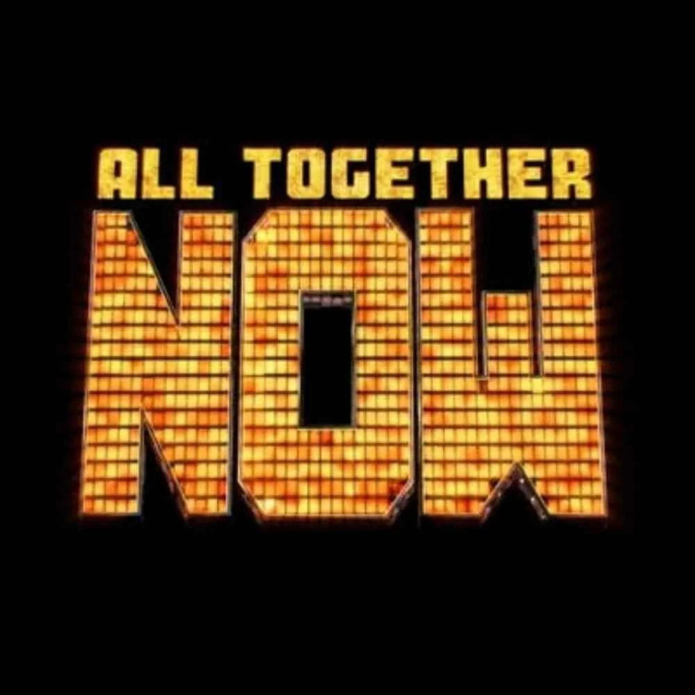 Illuminated sign with the words "All Together Now" in yellow text above a large illuminated marquee-style word "NOW" in orange and yellow lights on a black background.