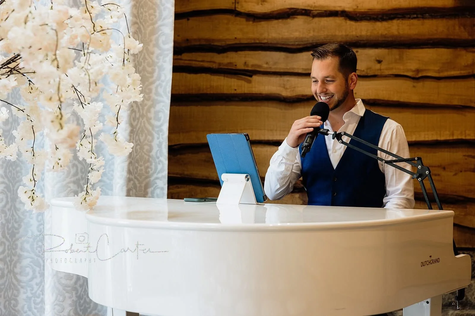 A man singing into a microphone while playing a white grand piano in a warmly decorated room.