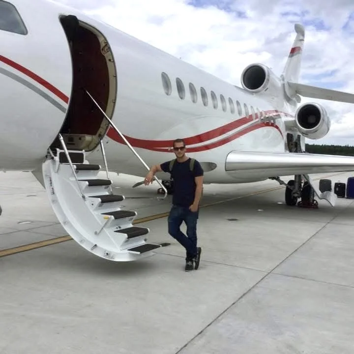 A man standing next to a private jet on an airport tarmac, with the jet's stairs extended.
