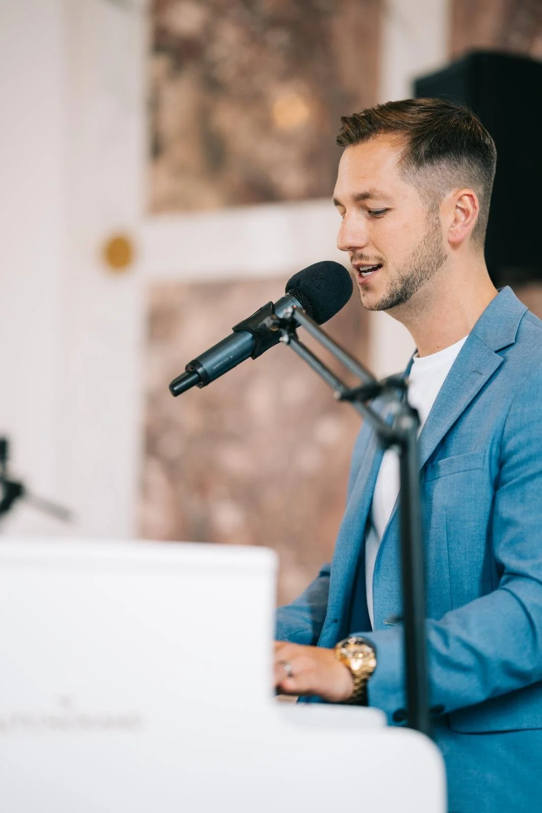 A man in a blue suit playing a white grand piano and singing into a microphone.