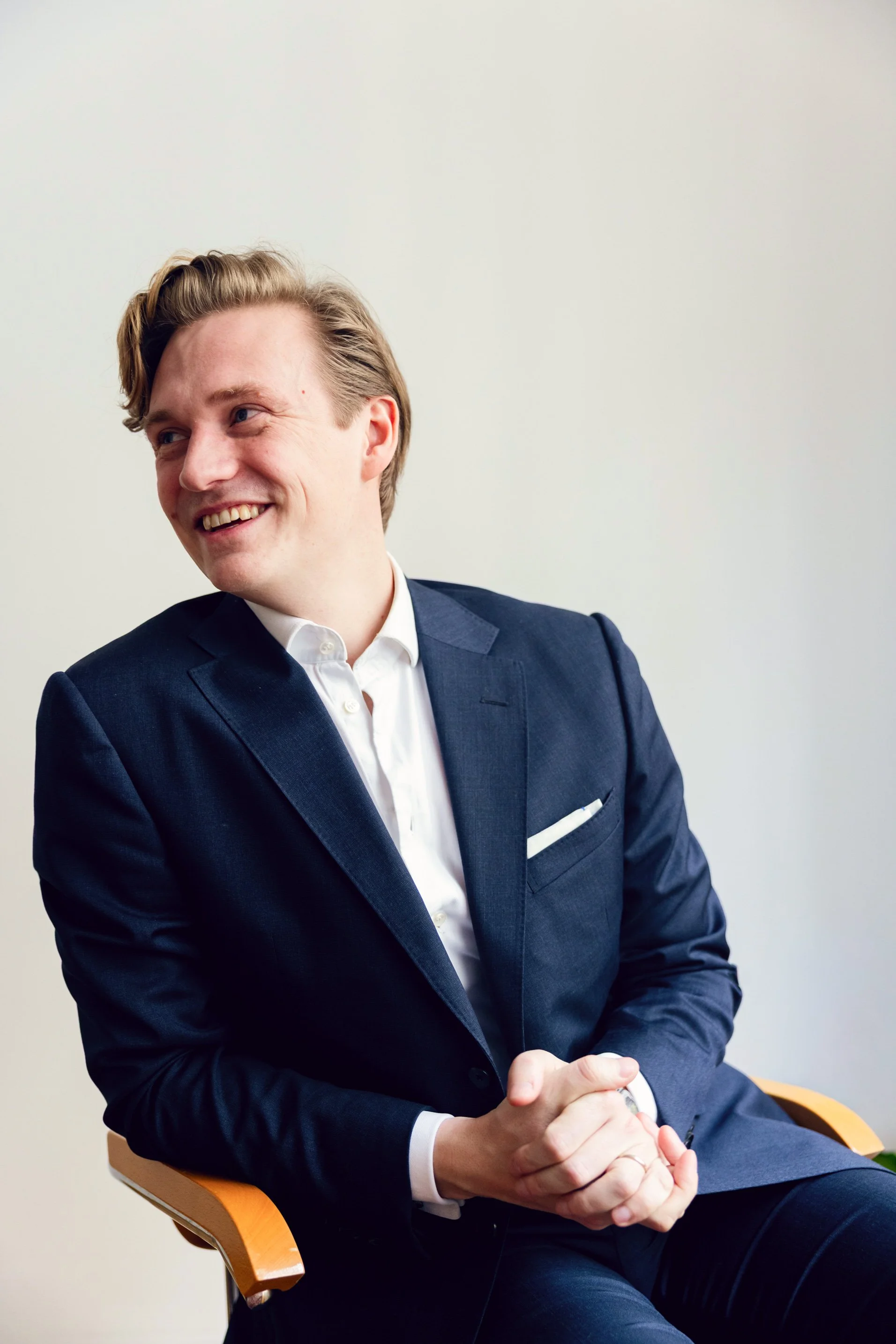 Portrait of Dominik Loidl sitting in a chair, smiling, wearing a dark blue suit.