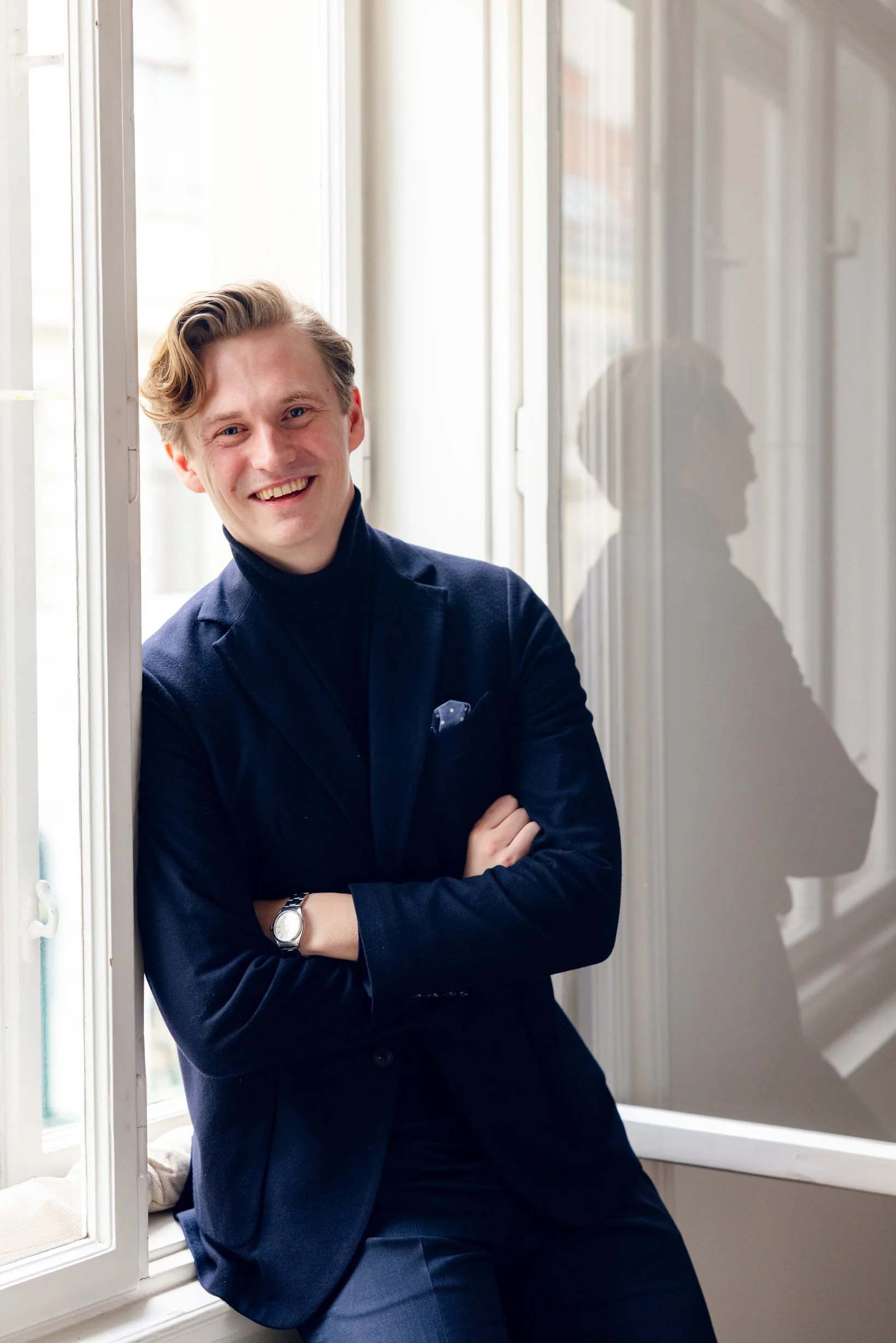 Dominik Loidl sitting at the window sill and smiling into the camera.