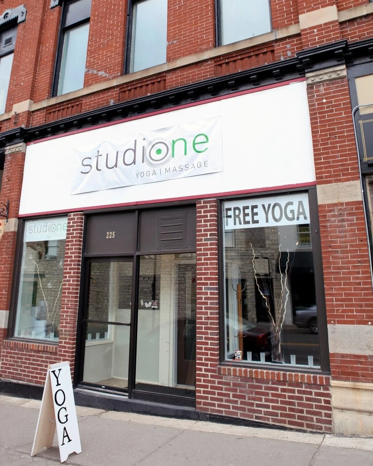 Exterior of a brick building with a sign Studio One Yoga and a FREE YOGA sign on the window, along with a sidewalk sign in Stillwater MN
