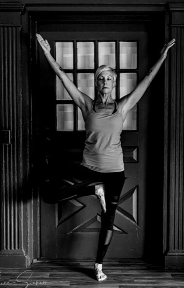 Woman with curly dark hair sitting on a bench in a minimalistic room with sunlight casting shadows and a wood-paneled wall.