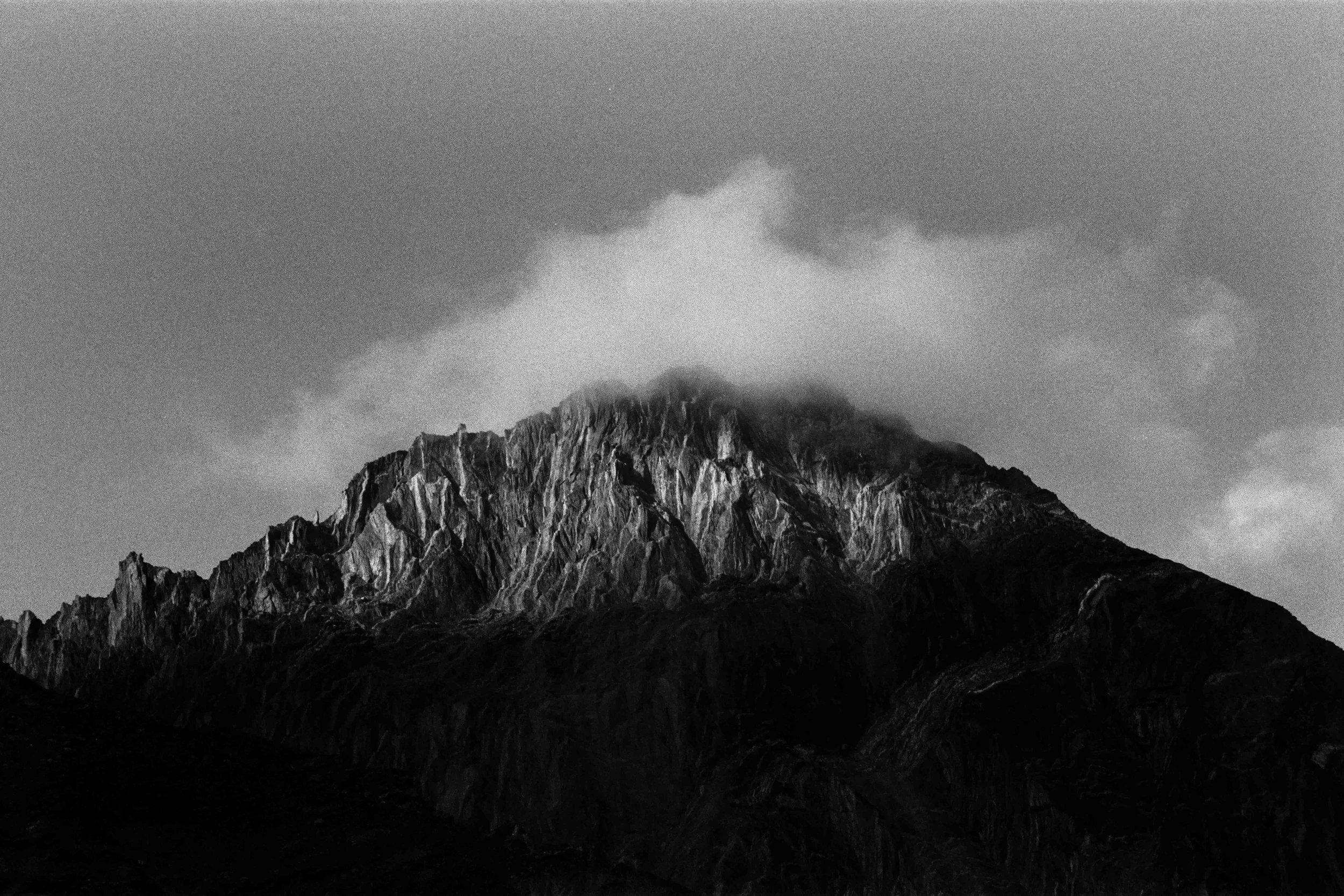 Montagne rocheuse avec un sommet partiellement couvert de nuages en noir et blanc.
