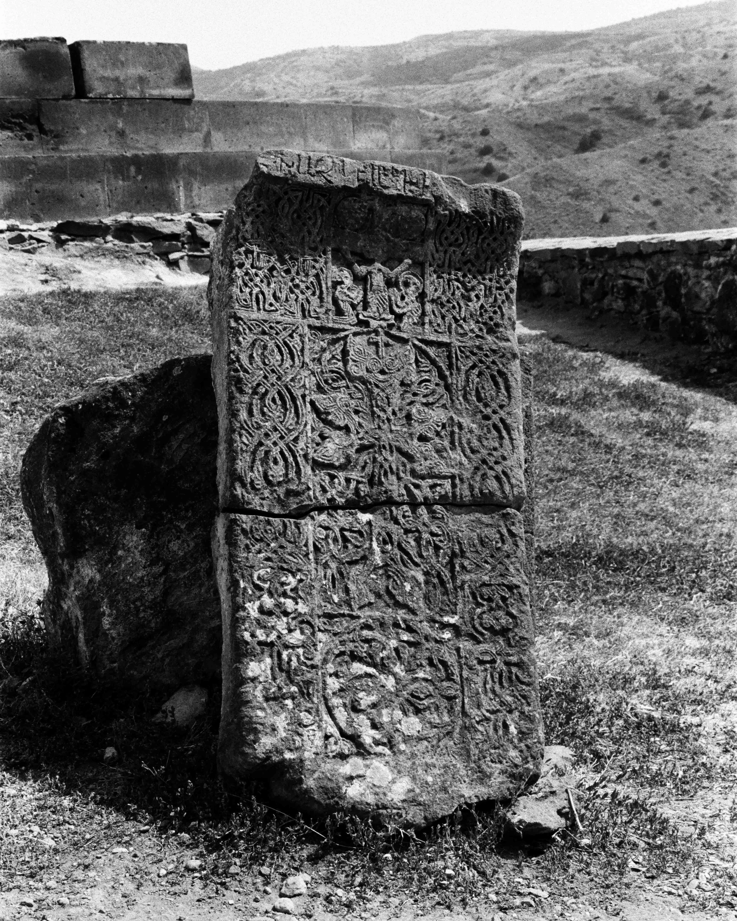 Pierre gravée avec des motifs et des symboles anciens, située dans un paysage de terrain rocheux et montagneux.