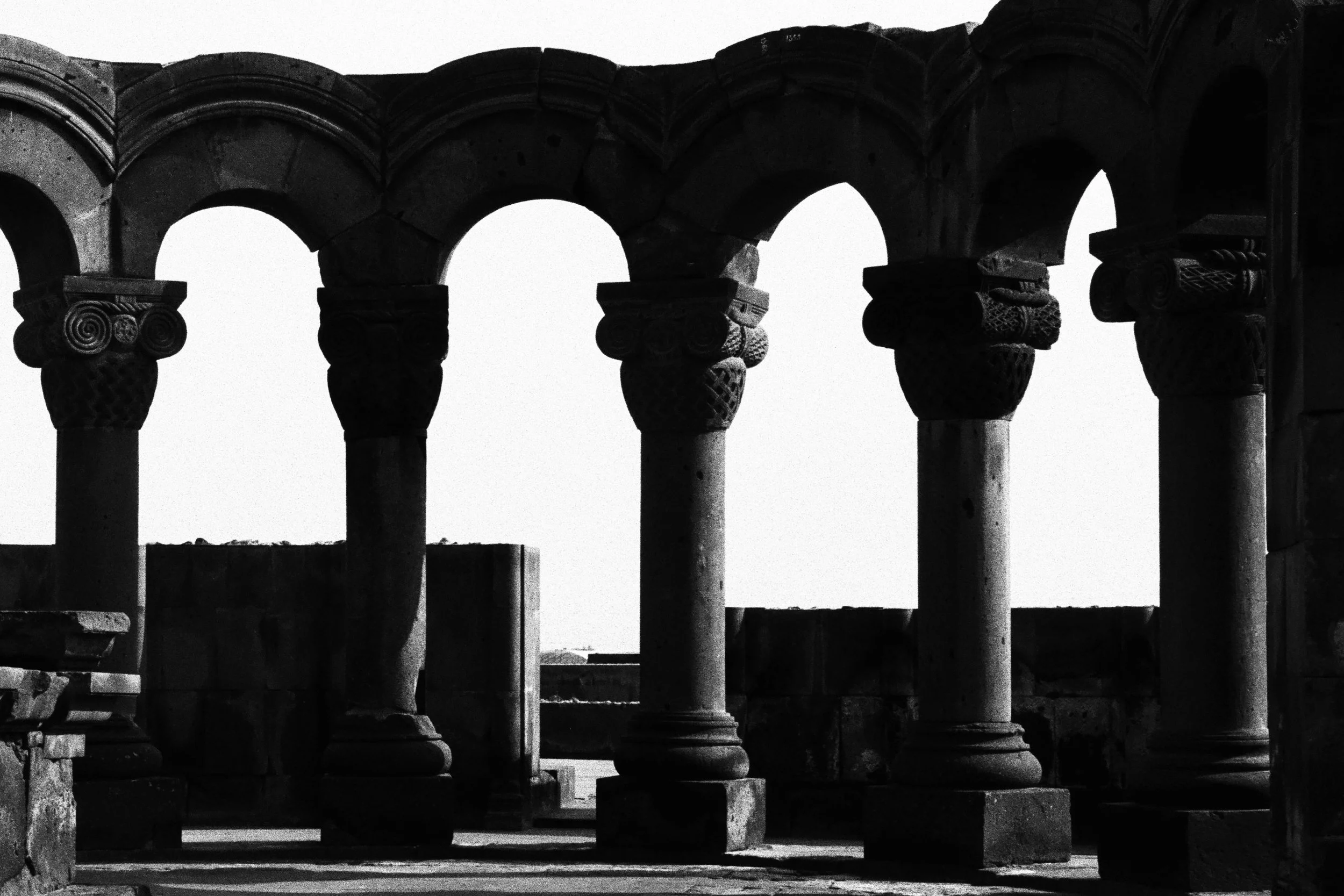 Colonnes de pierre anciennes avec chapiteaux sculptés sous un arc de pierre, vue en silhouette