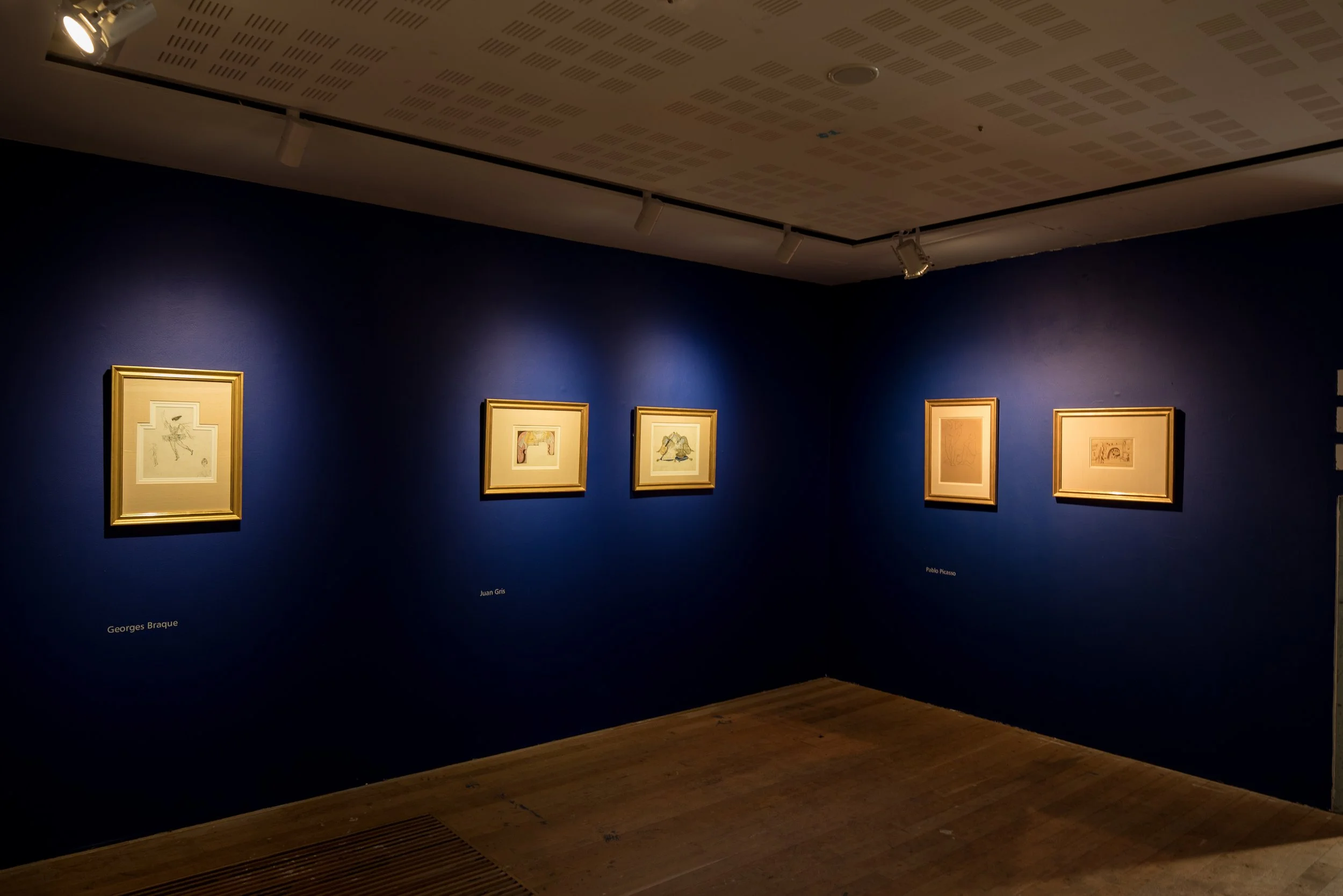 Gallery with five framed sketches hanging on a dark blue wall, with labels underneath each frame, in an art museum.