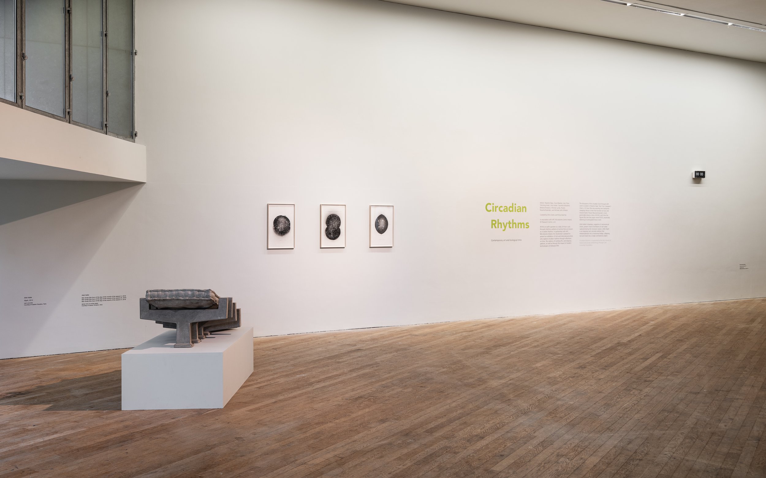 Art gallery interior featuring three framed black and white abstract prints labeled 'Circadian Rhythms' on the wall, with a modern sculpture on a white pedestal and informational text on the nearby wall.
