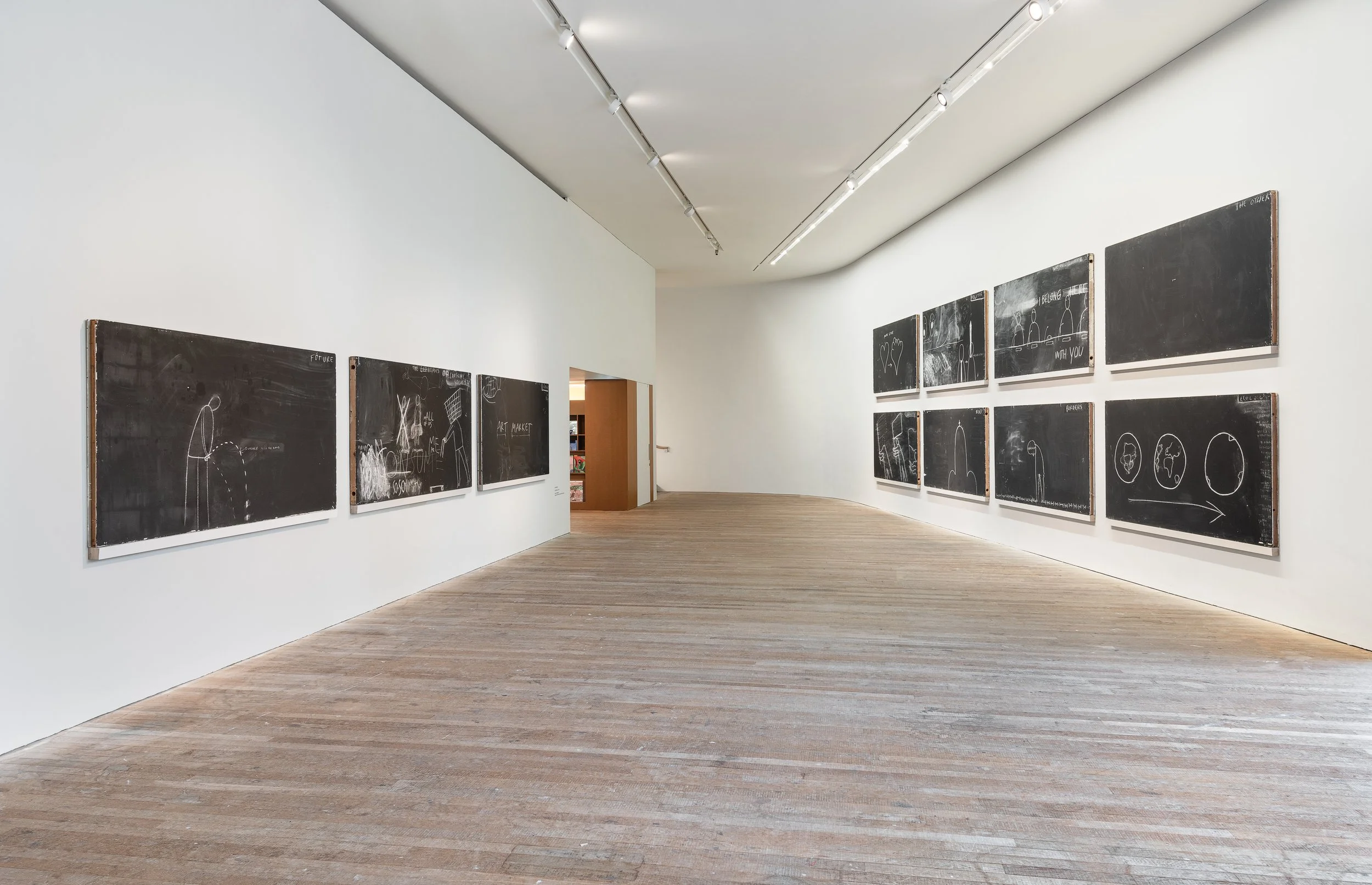 Gallery with ten blackboards displaying white chalk drawings and words, featuring sketches of shapes, figures, and text in an art museum exhibit.
