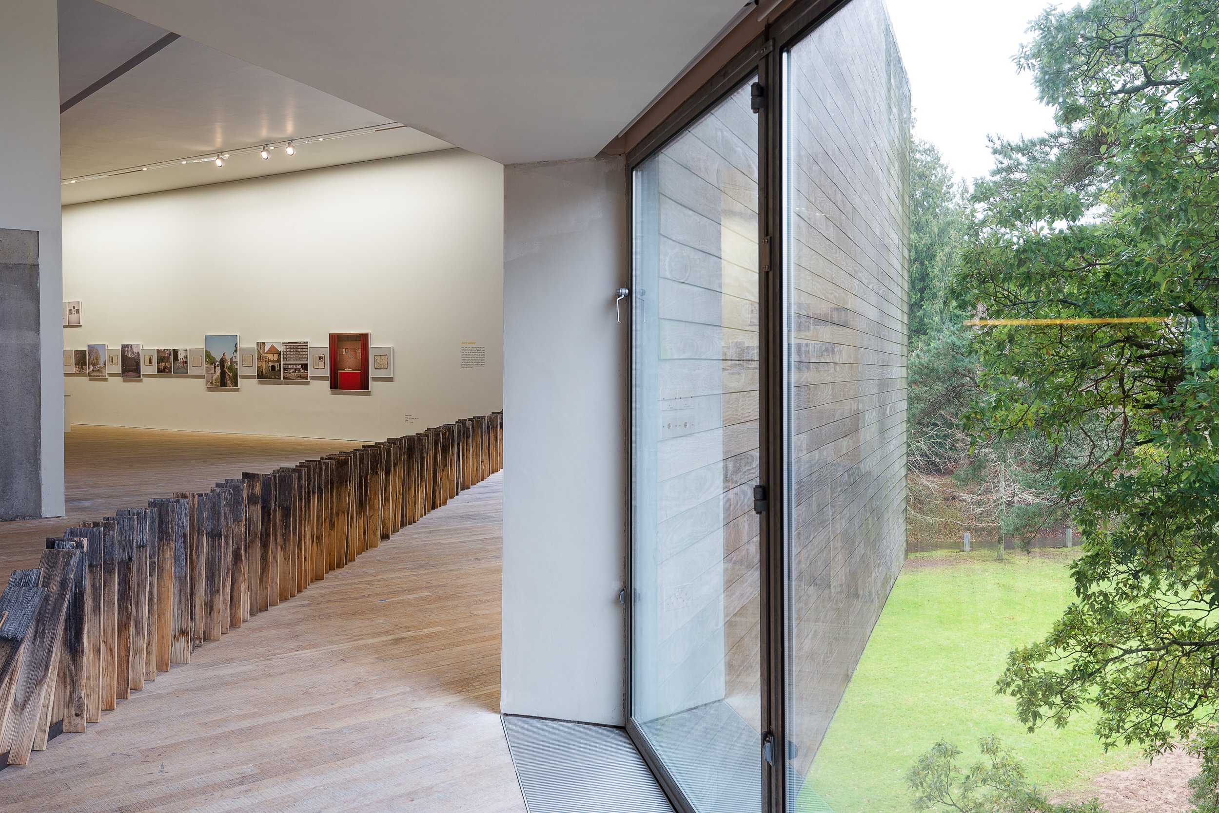 View from an art gallery with a wooden barrier and a large window showing greenery outside.