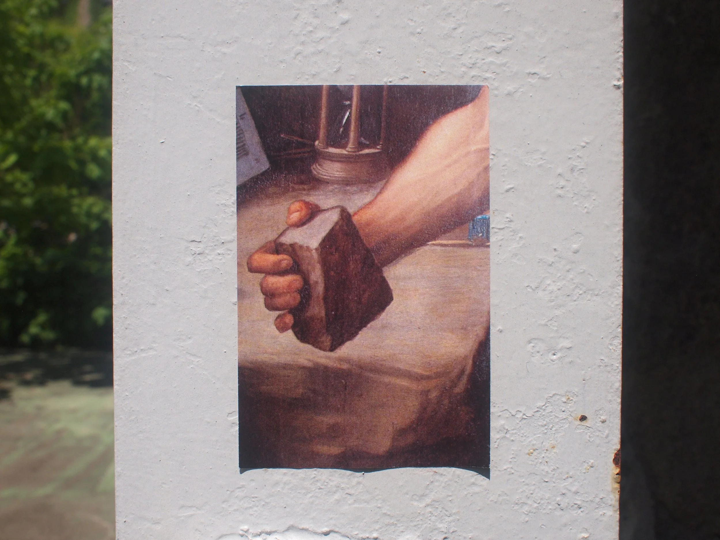 A person holding a dark brown rock with their right hand on a wooden surface, with a metal object in the background.