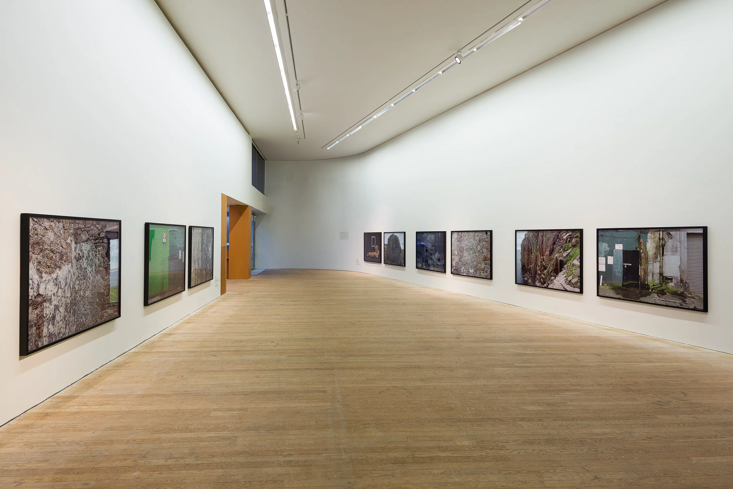 Art gallery with framed photographs on white walls and wooden flooring.