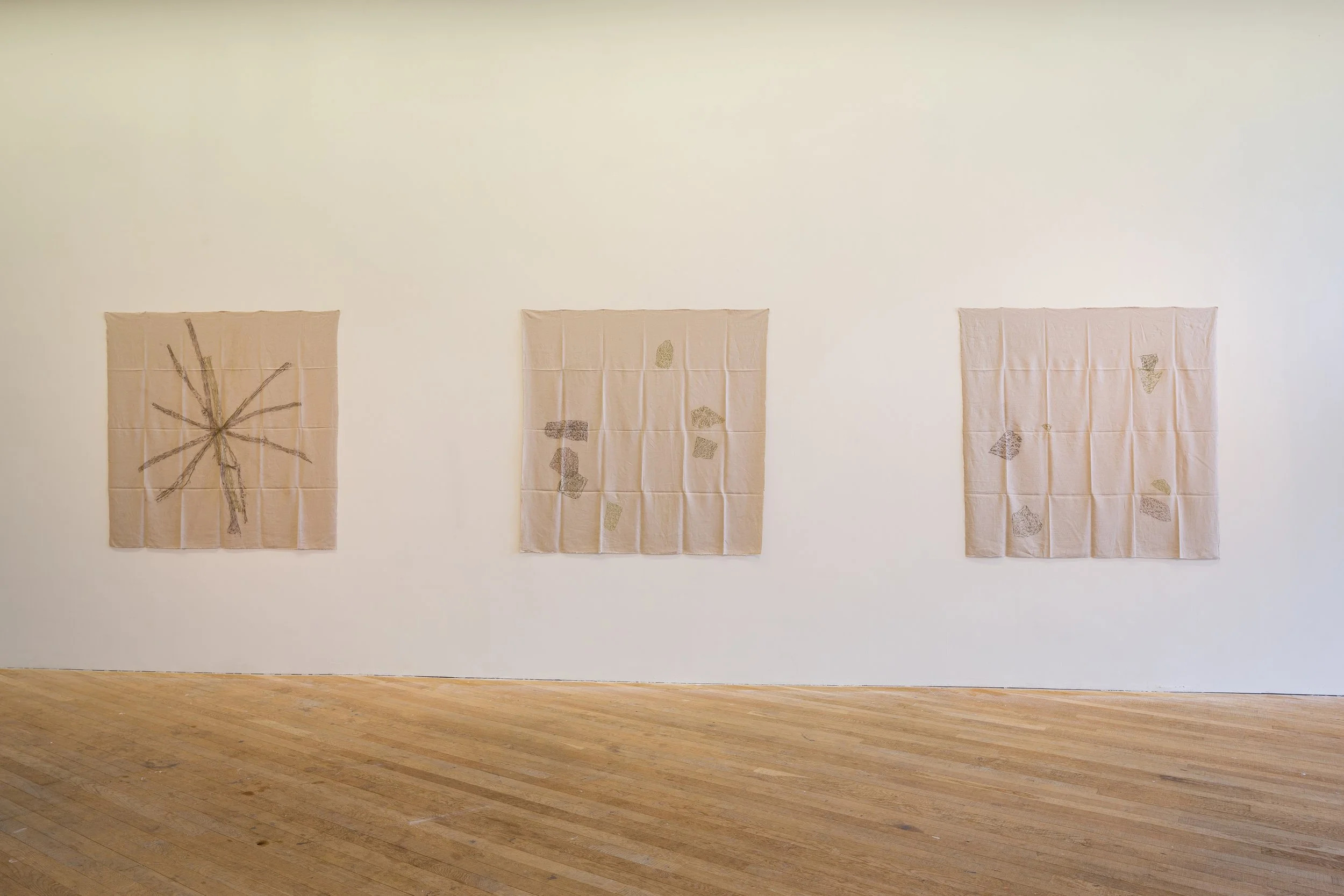 Three large fabric art pieces with abstract designs hanging on a white wall in an art gallery with wooden floors.