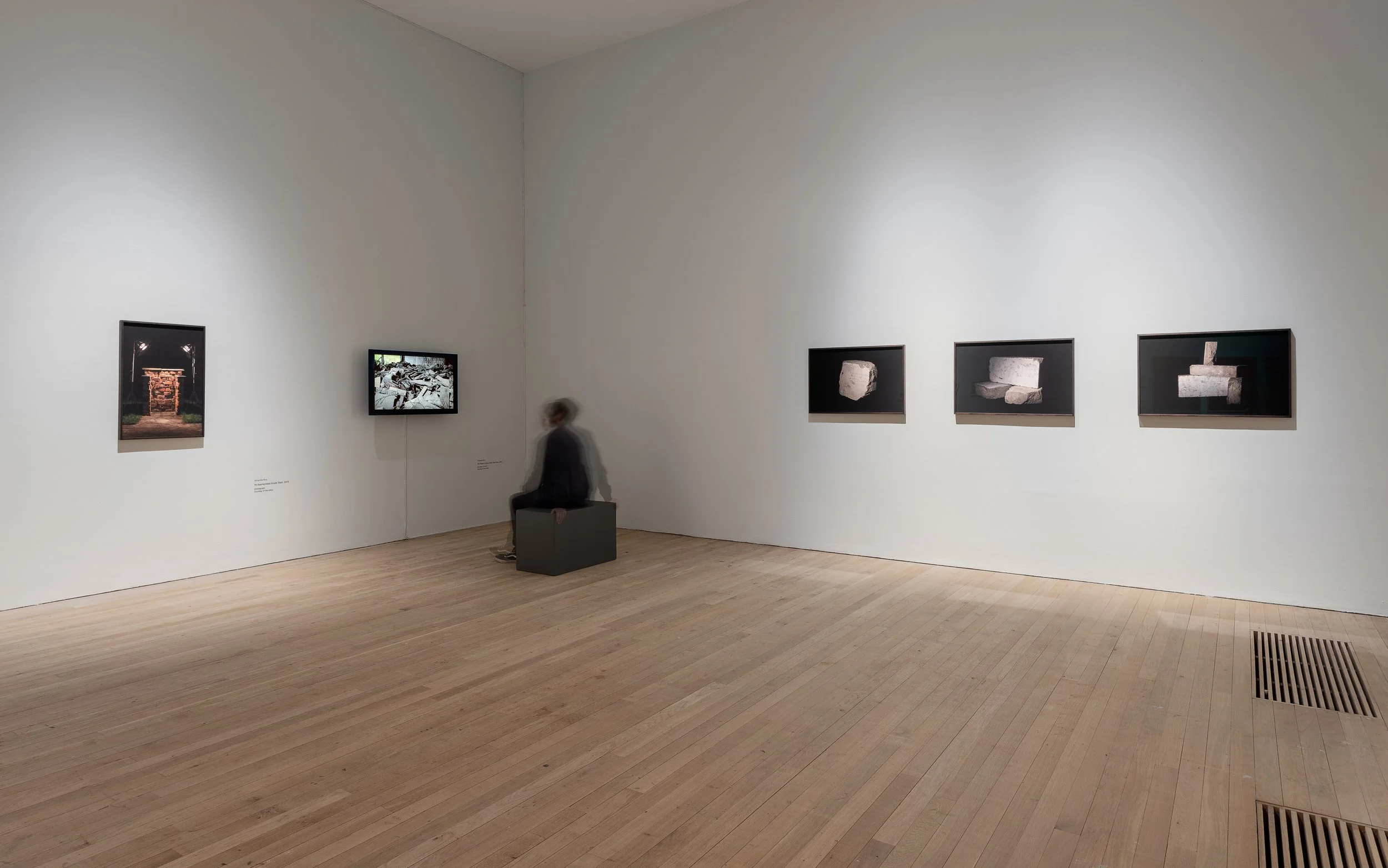 Gallery with artworks on the wall and a person sitting on a bench.