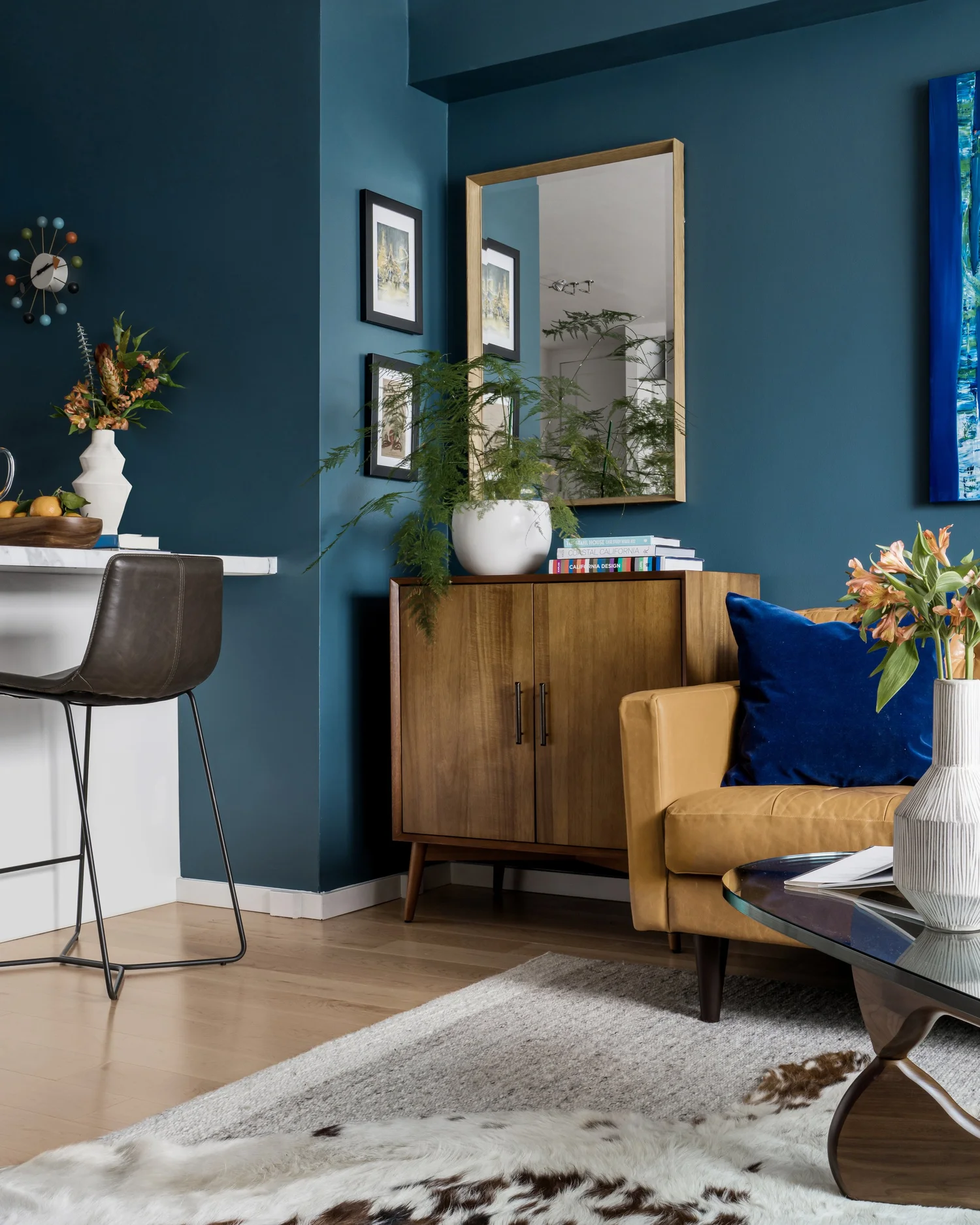 Walnut credenza, round mirror and counter stools against the teal wall