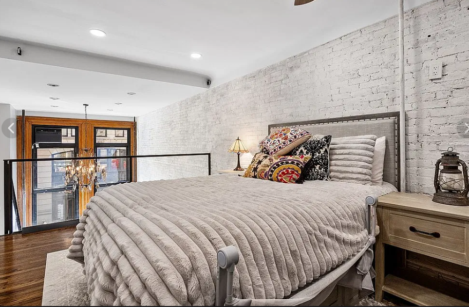 Loft sleeping area before: upholstered bed and patterned pillows against whitewashed brick