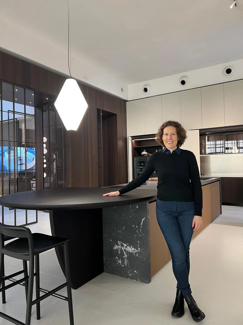 Melissa Pinson in a Milan kitchen showroom, beside a black marble and dark wood island
