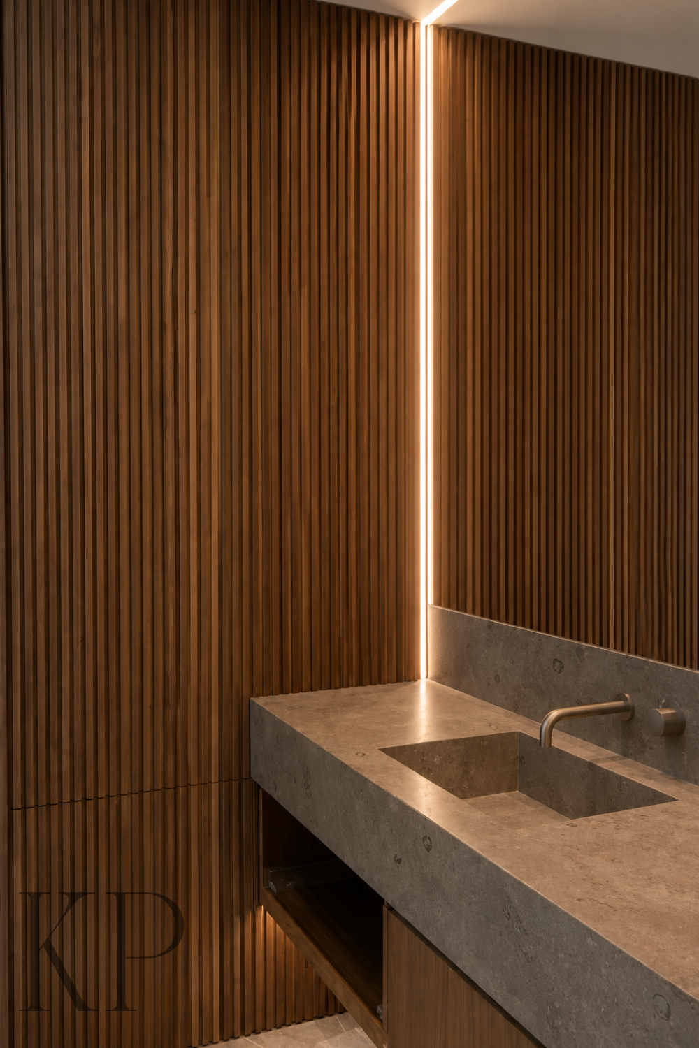Interior of a modern room featuring vertical wooden slats on the wall, a concrete countertop with a built-in sink, metallic faucet, and warm vertical lighting accentuating the corner.