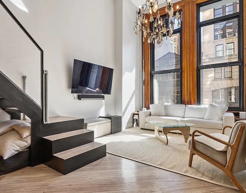 Loft living room before: white sofa, glass coffee table and chandelier beside tall windows