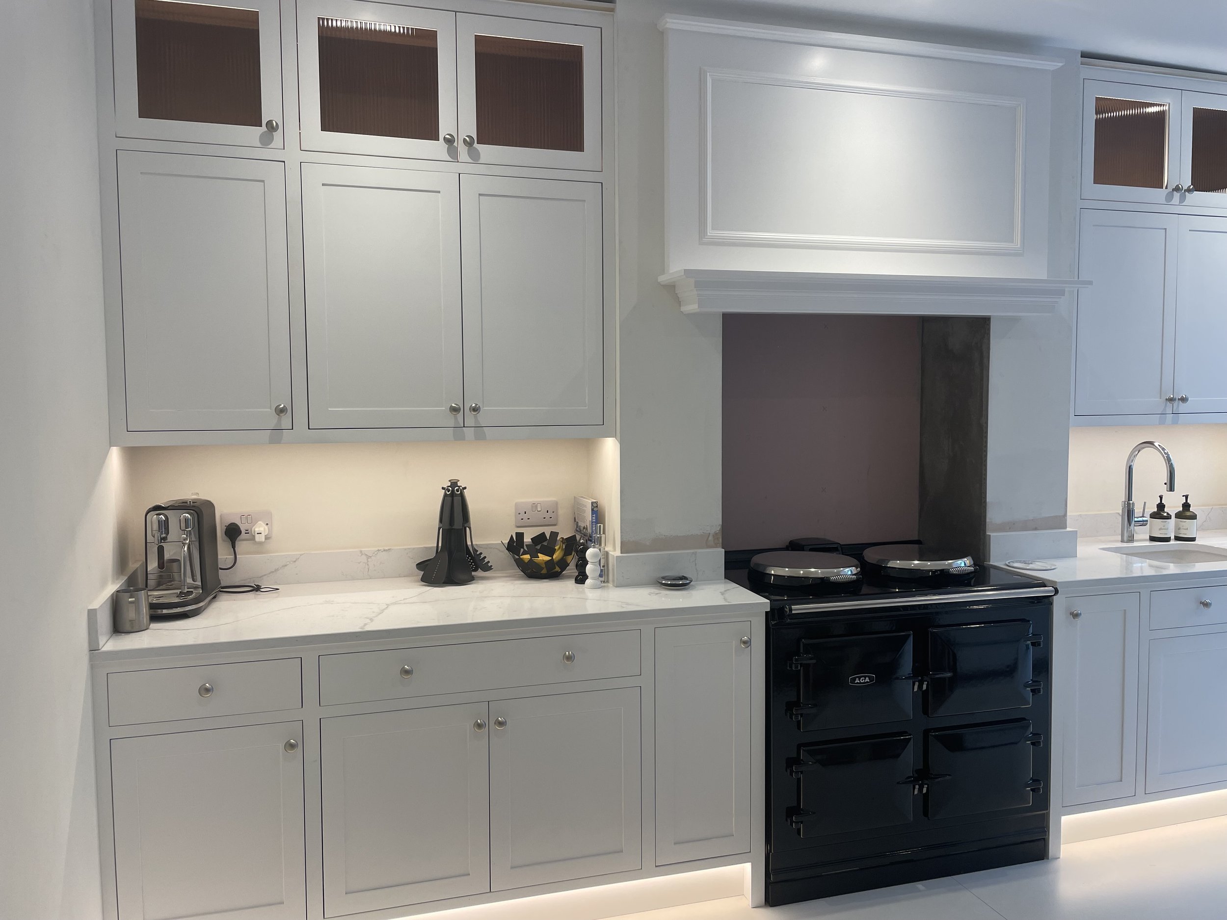 Modern kitchen with white cabinetry, marble countertops, black range oven, coffee machine, soap dispensers, and small appliances.