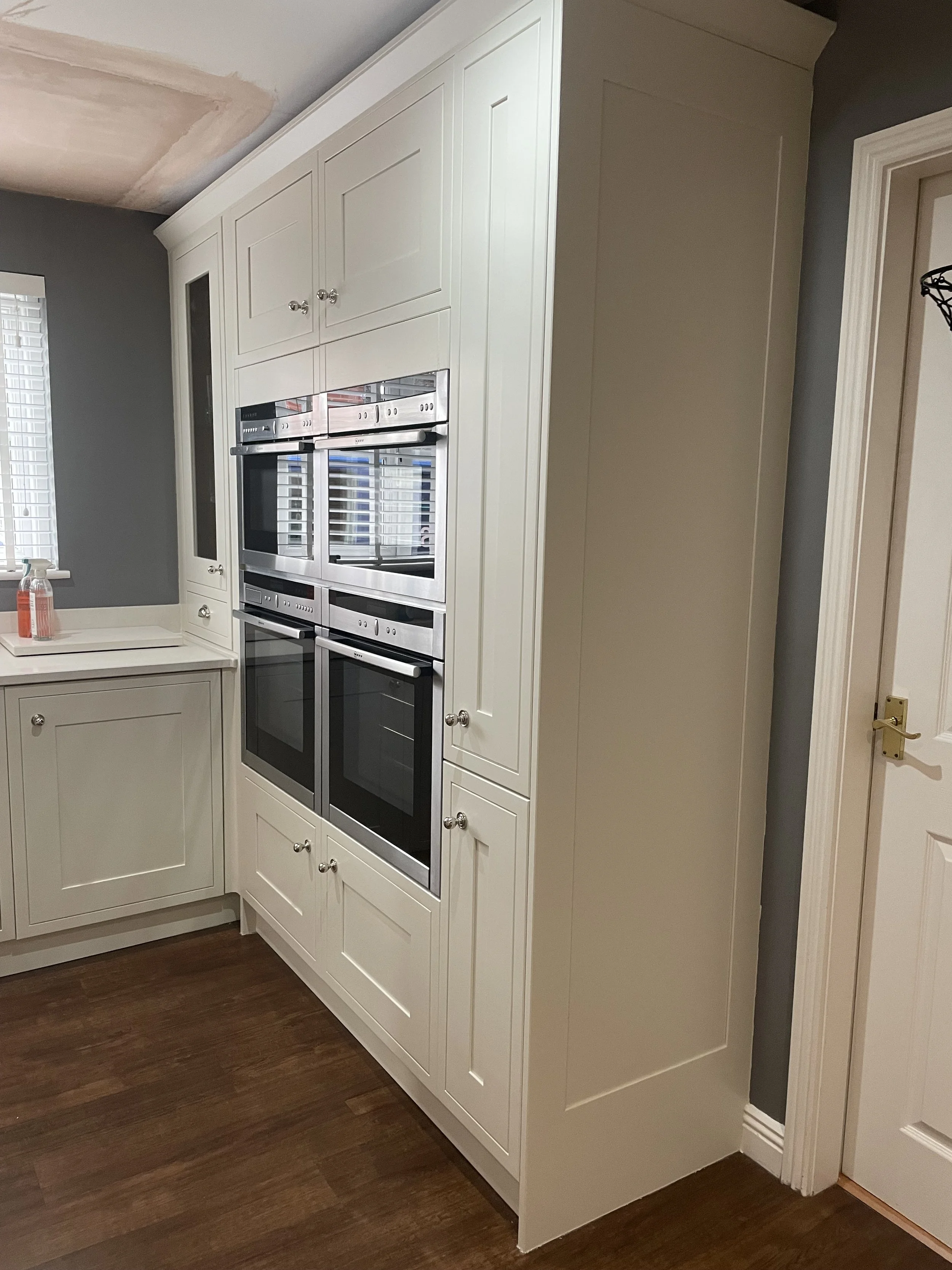 Kitchen with white cabinetry, built-in stainless steel double ovens, and dark hardwood floors.