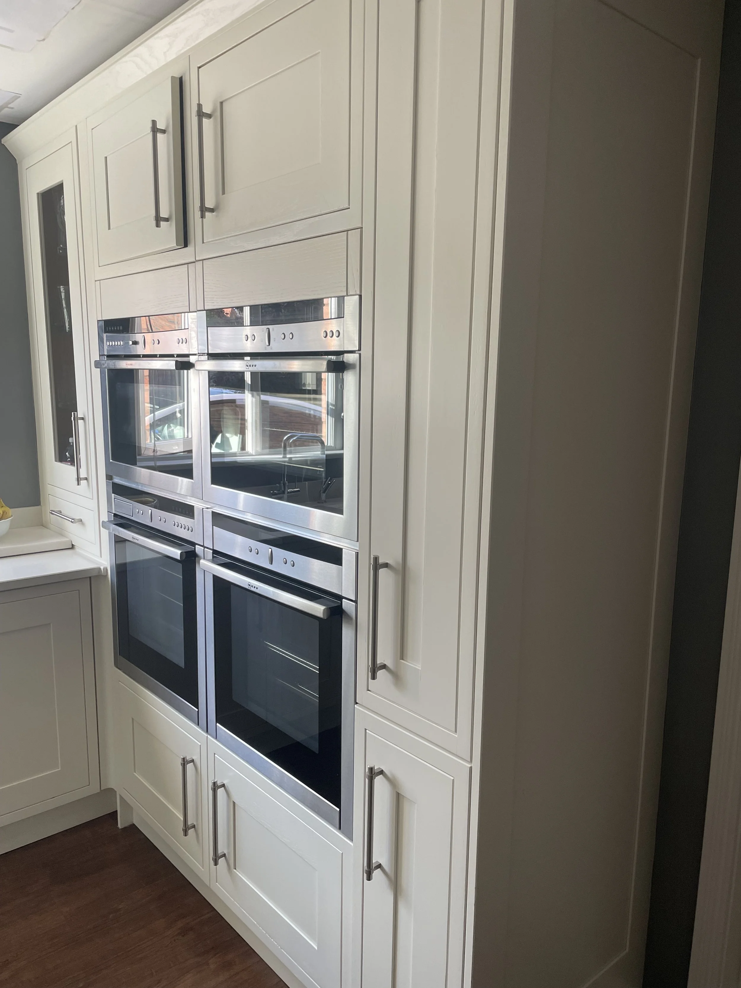 A built-in kitchen oven and microwave with stainless steel surfaces, surrounded by white cabinetry with silver handles.