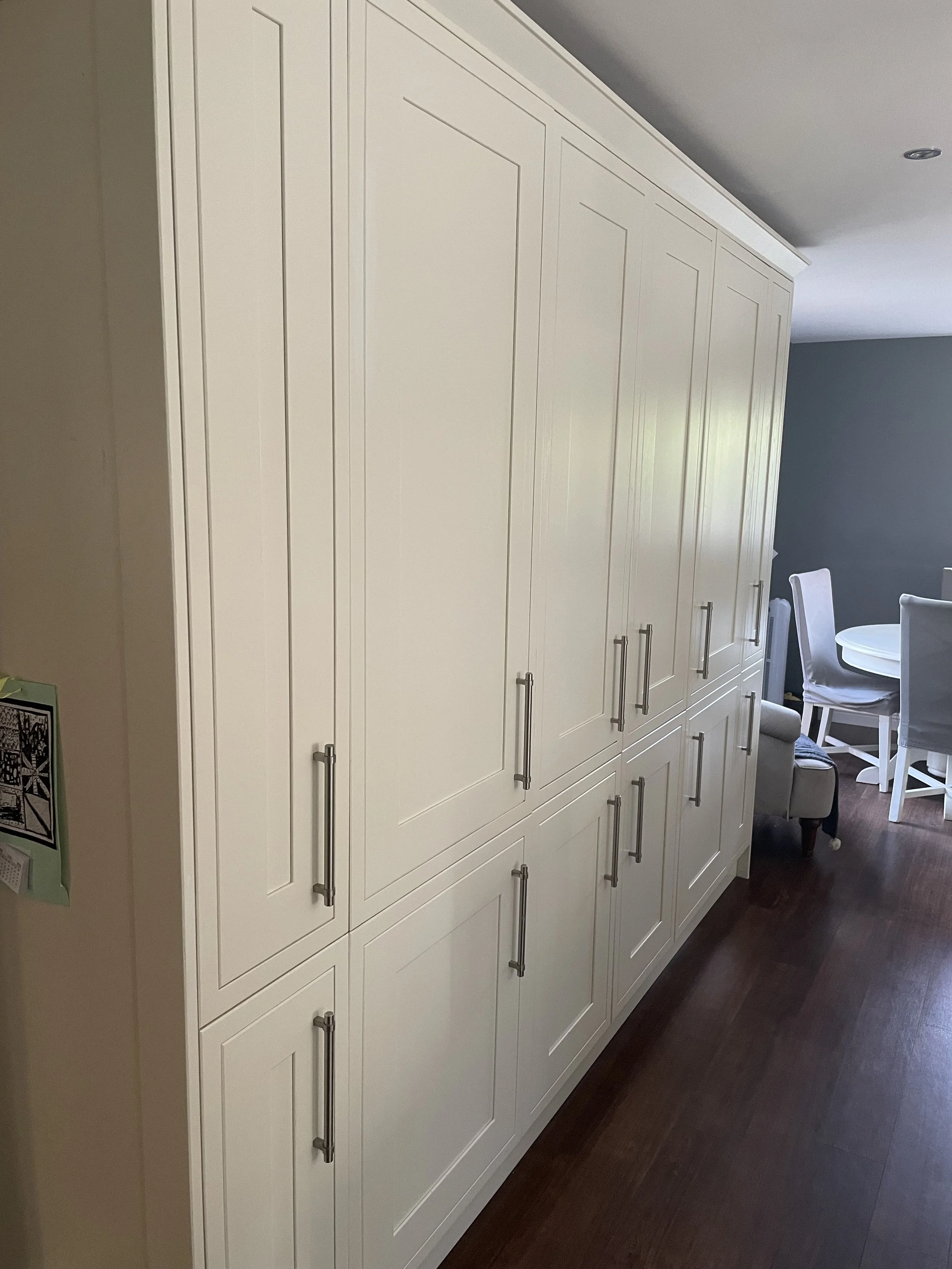 White kitchen cabinets with silver handles in a modern home, visible in a room with a dining area and hardwood floor.